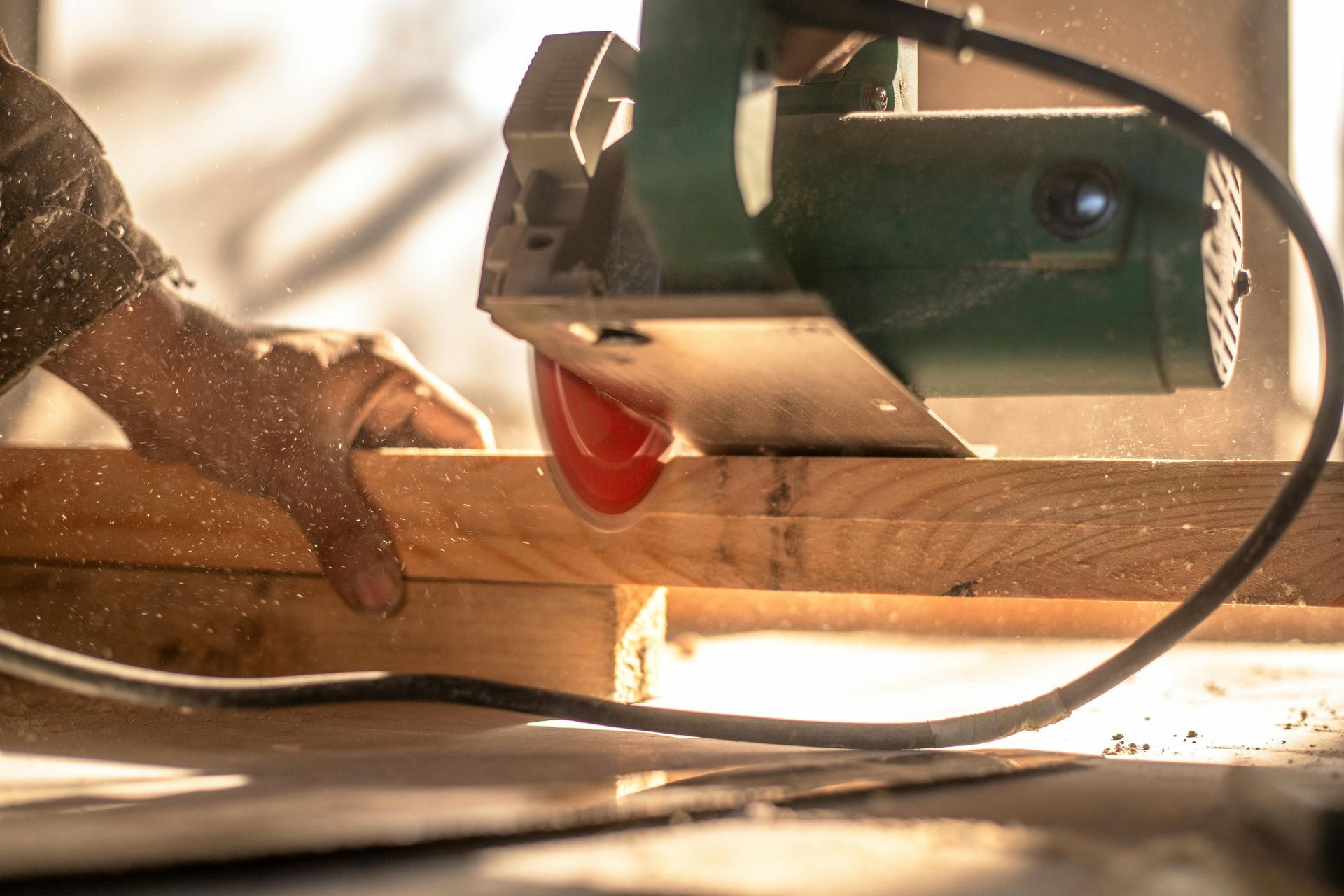 Hands guiding a circular saw cutting wood, with sawdust flying in a workshop