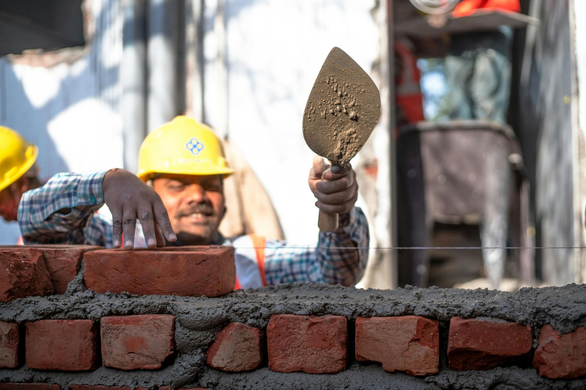 Construction worker in yellow hard hat laying bricks on a wall with a trowel