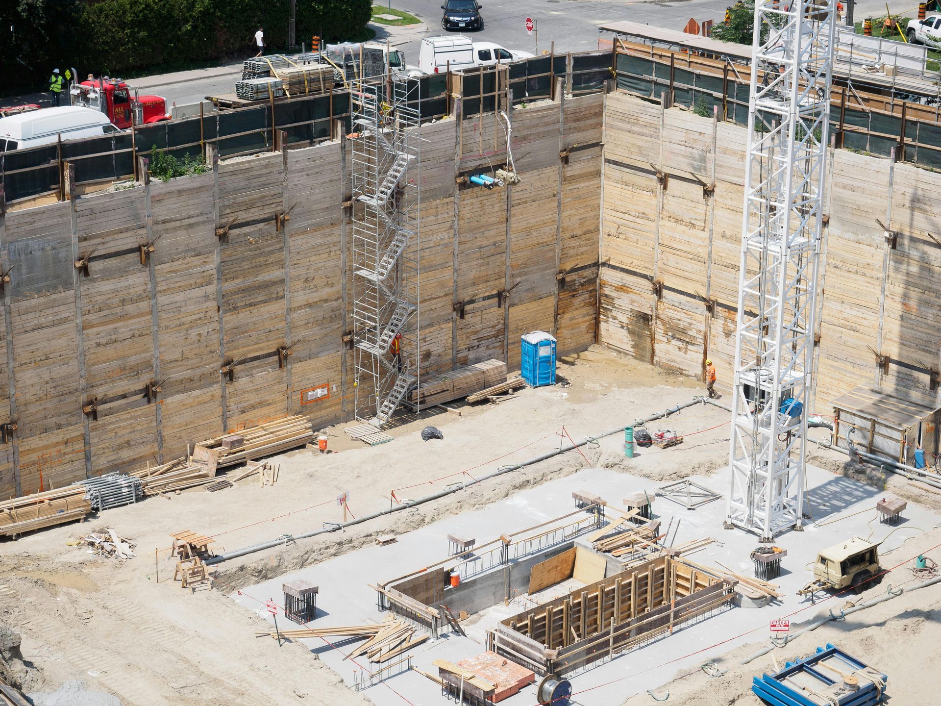 Deep construction pit with concrete walls, scaffolding, and equipment at an urban site