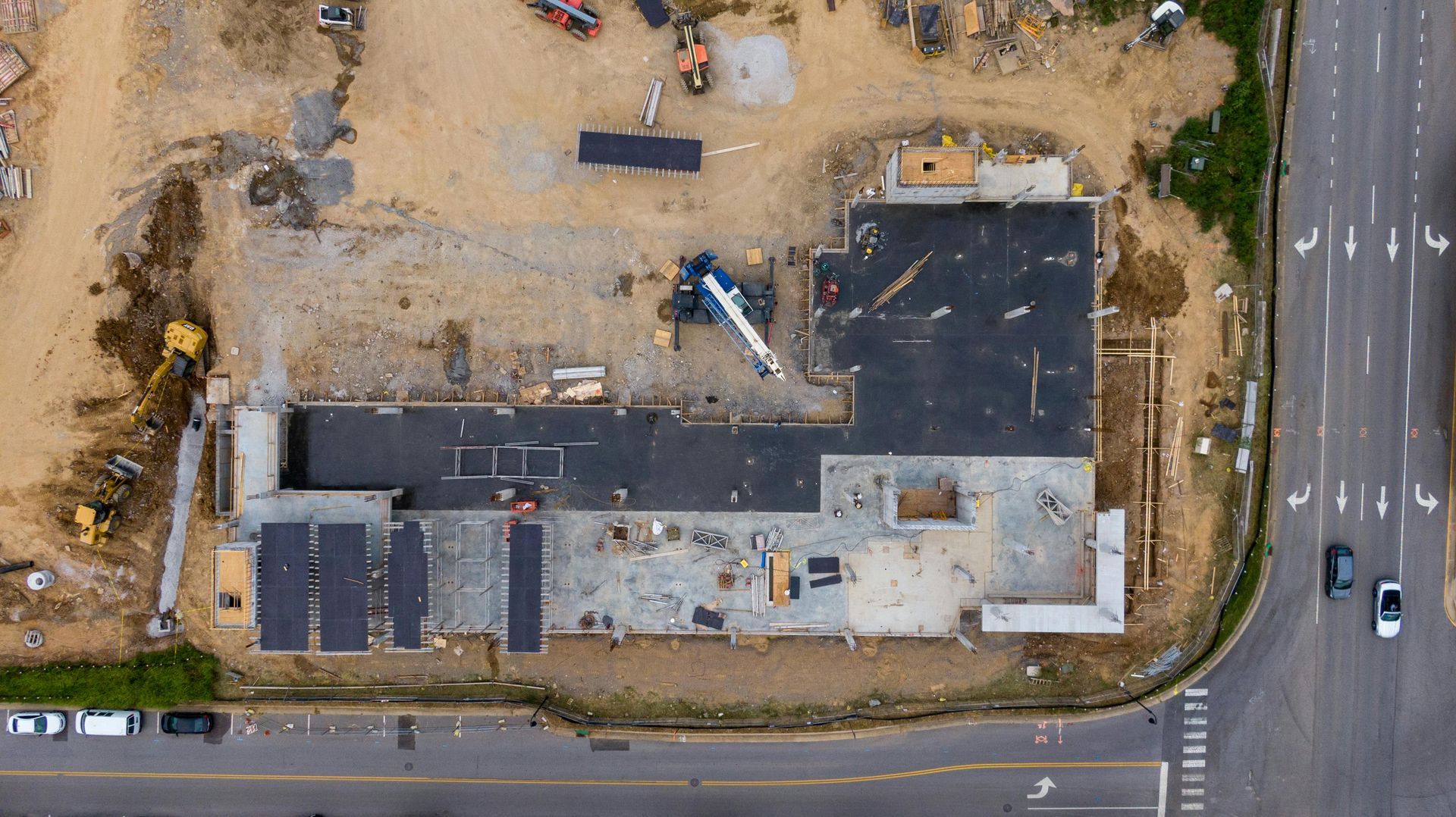 Aerial view of a construction site with heavy equipment, paved roads, and a partially built structure.