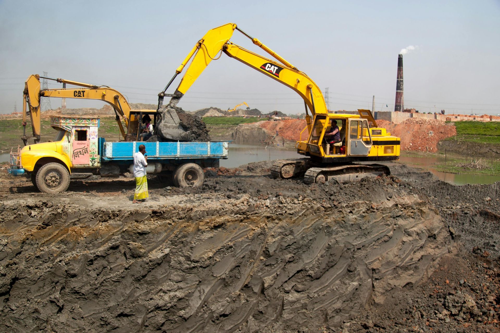 Excavators loading dirt into a blue truck at a construction site under clear skies