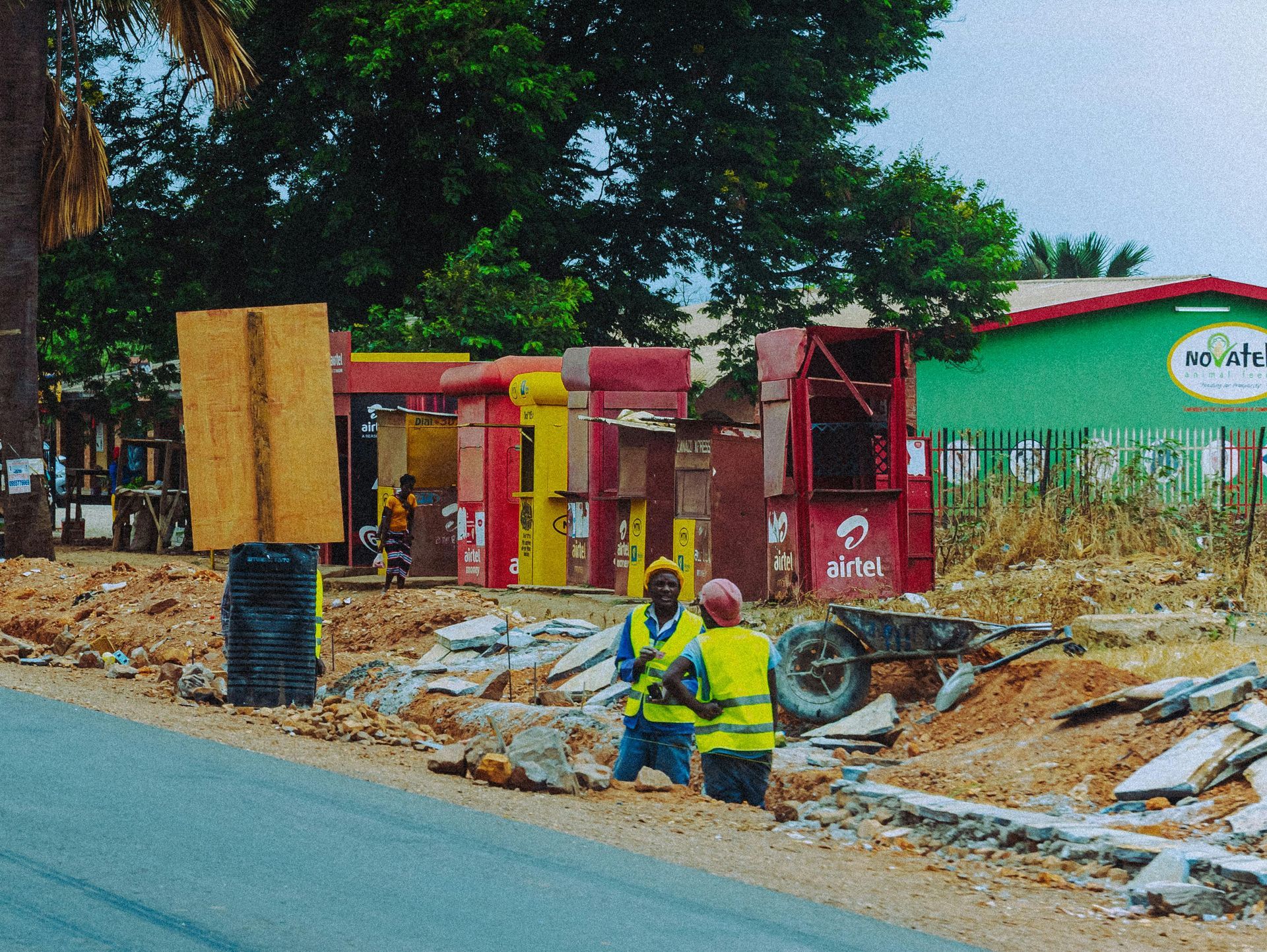 Roadside utility workers in yellow vests near a red kiosk and debris by a paved street