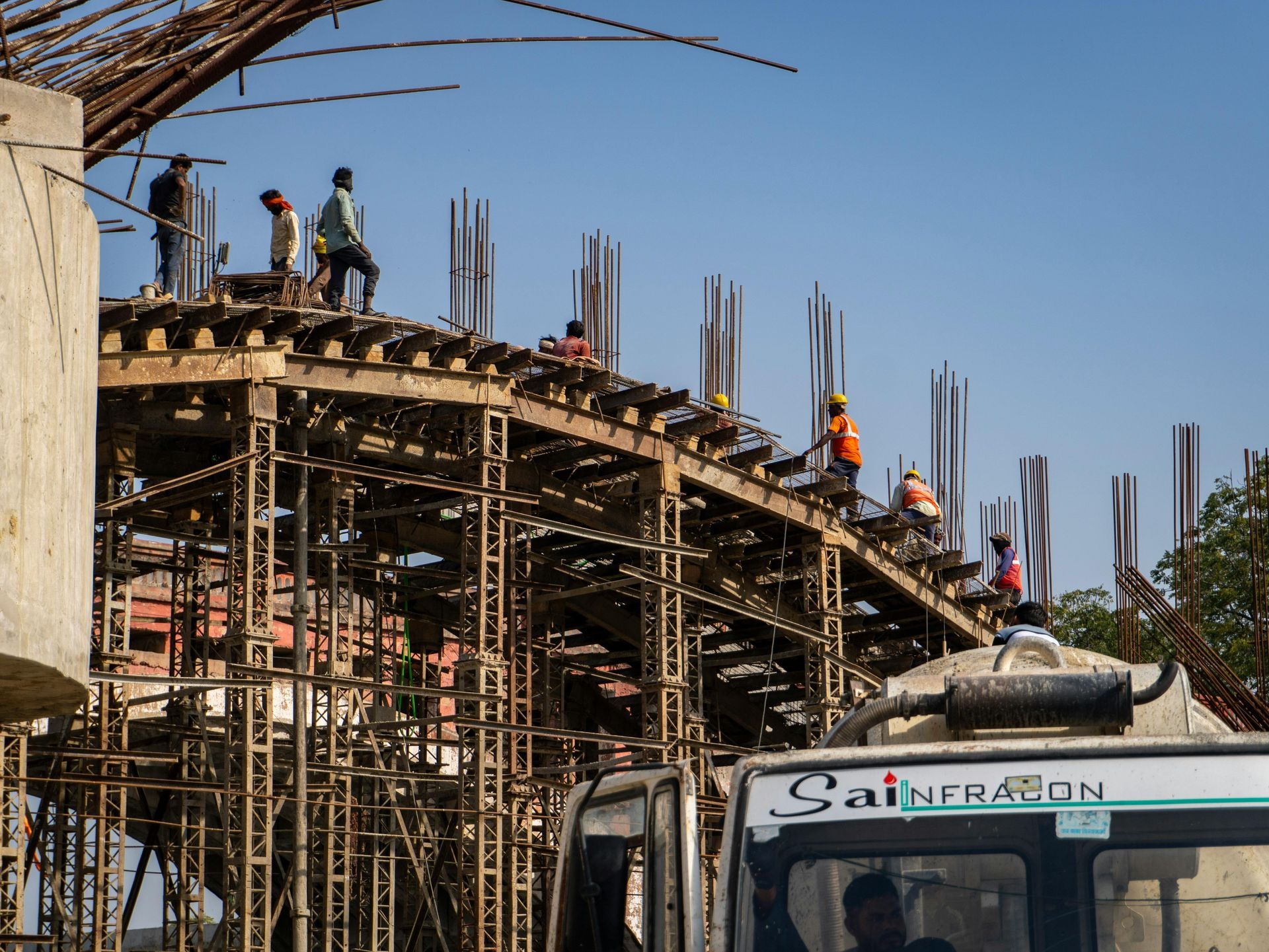 Construction workers on scaffolding building a curved concrete structure beside a truck under a blue sky
