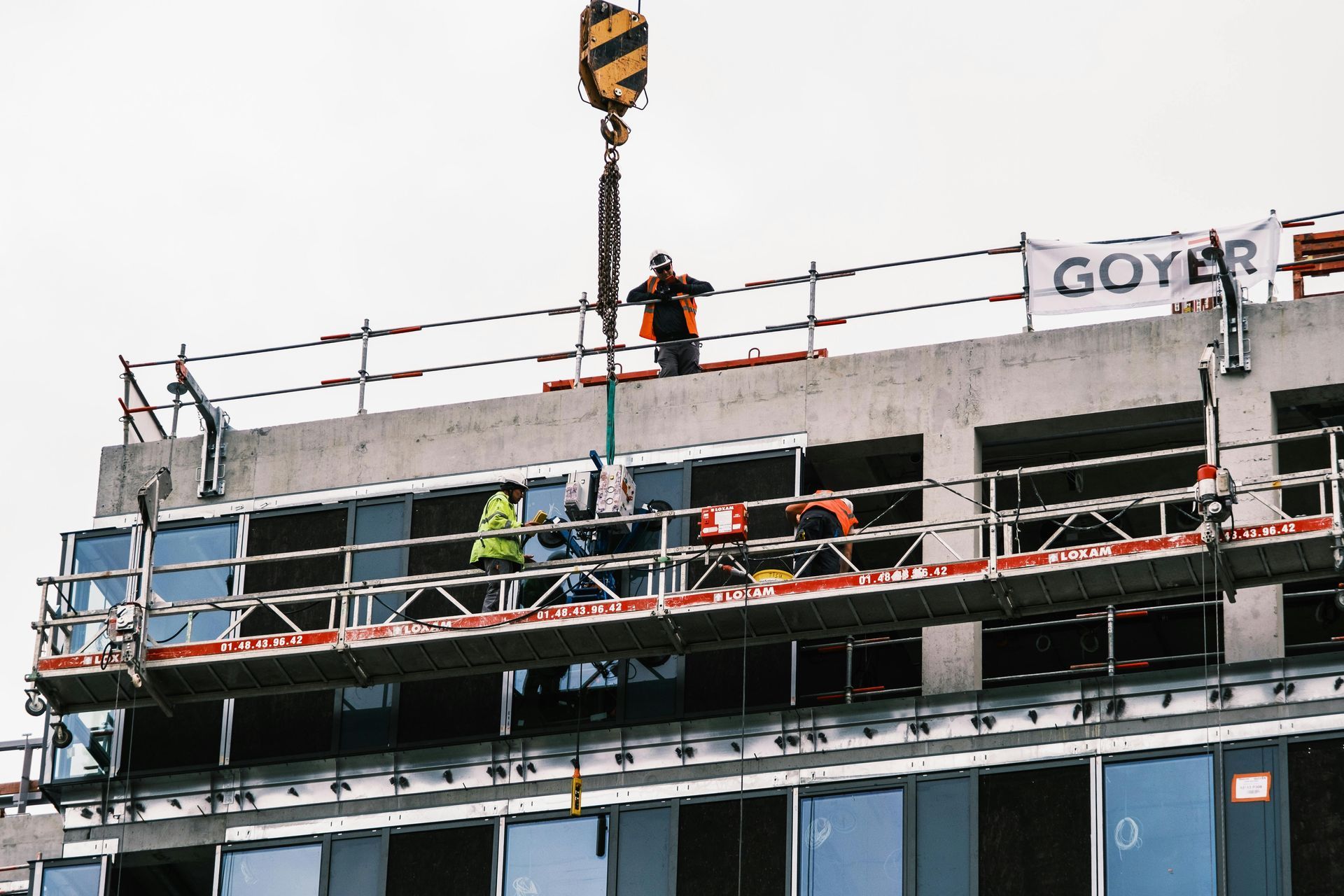 Worker on scaffolding at a building under construction, with a crane above.