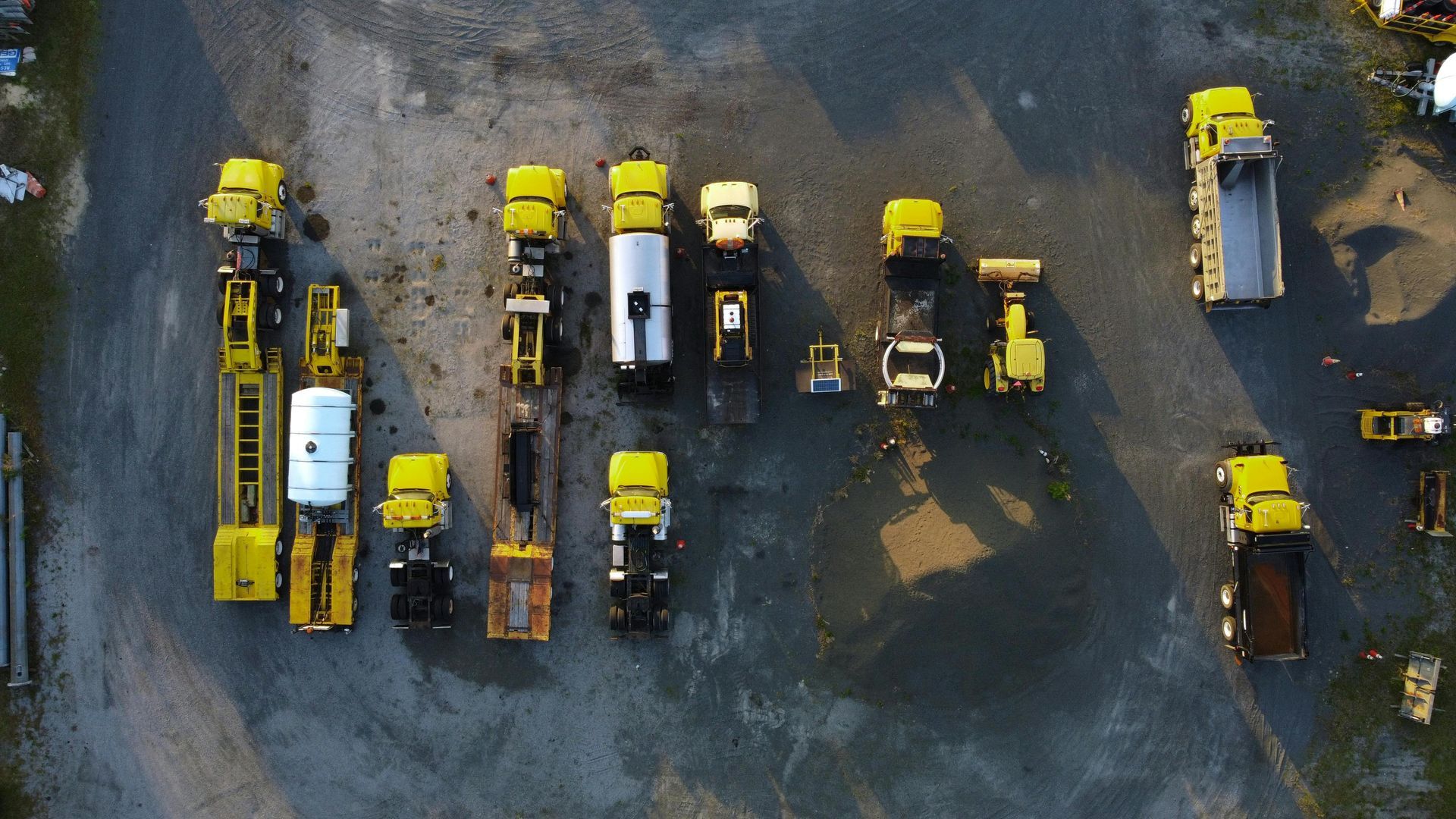 Aerial view of several yellow and white construction vehicles parked on muddy ground.
