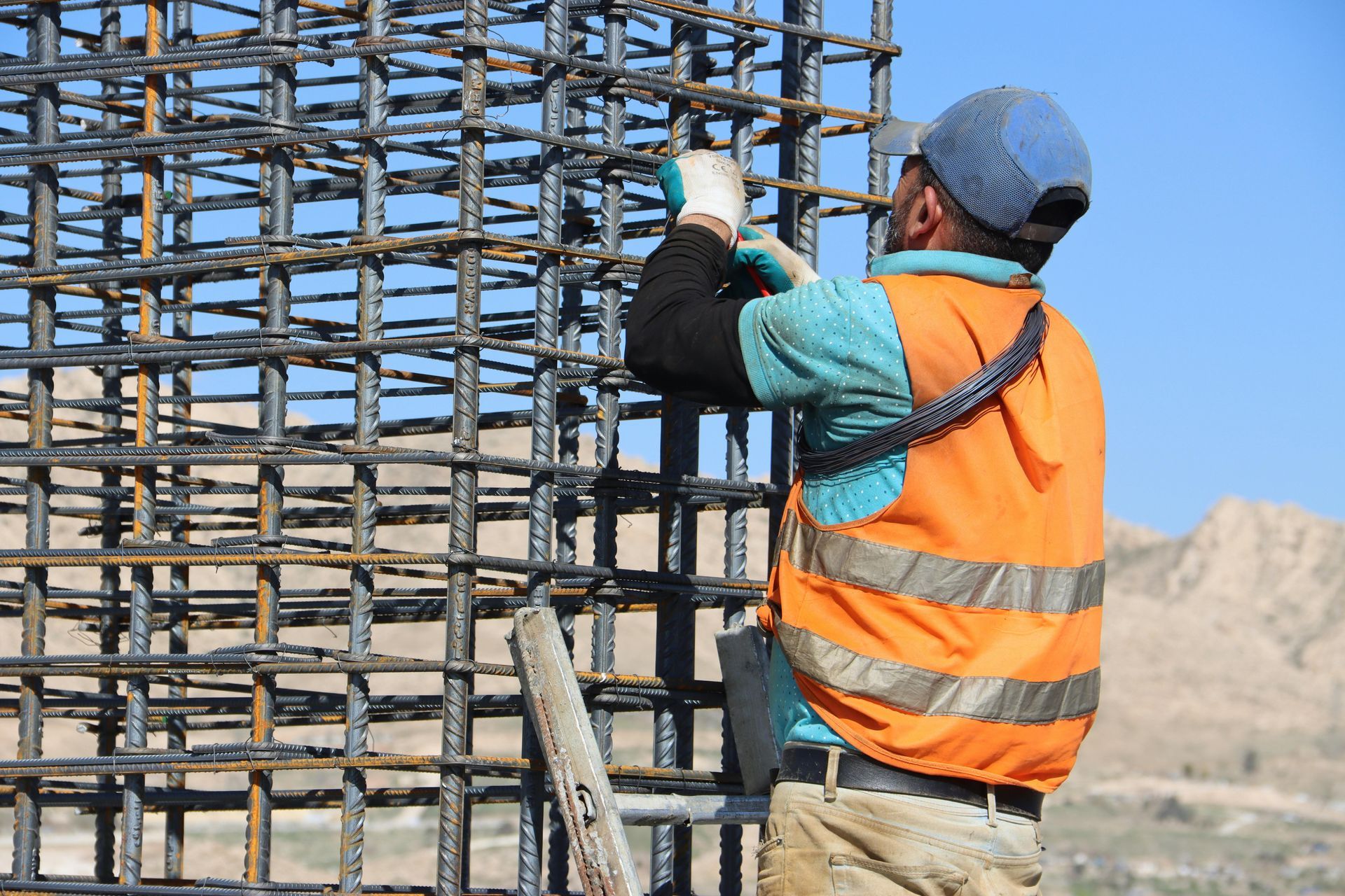 Construction worker in orange vest tying rebar on a building frame outdoors