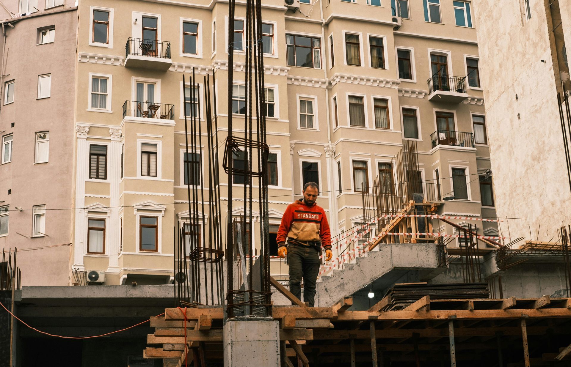 Construction worker in red jacket standing on a scaffold in front of apartment buildings