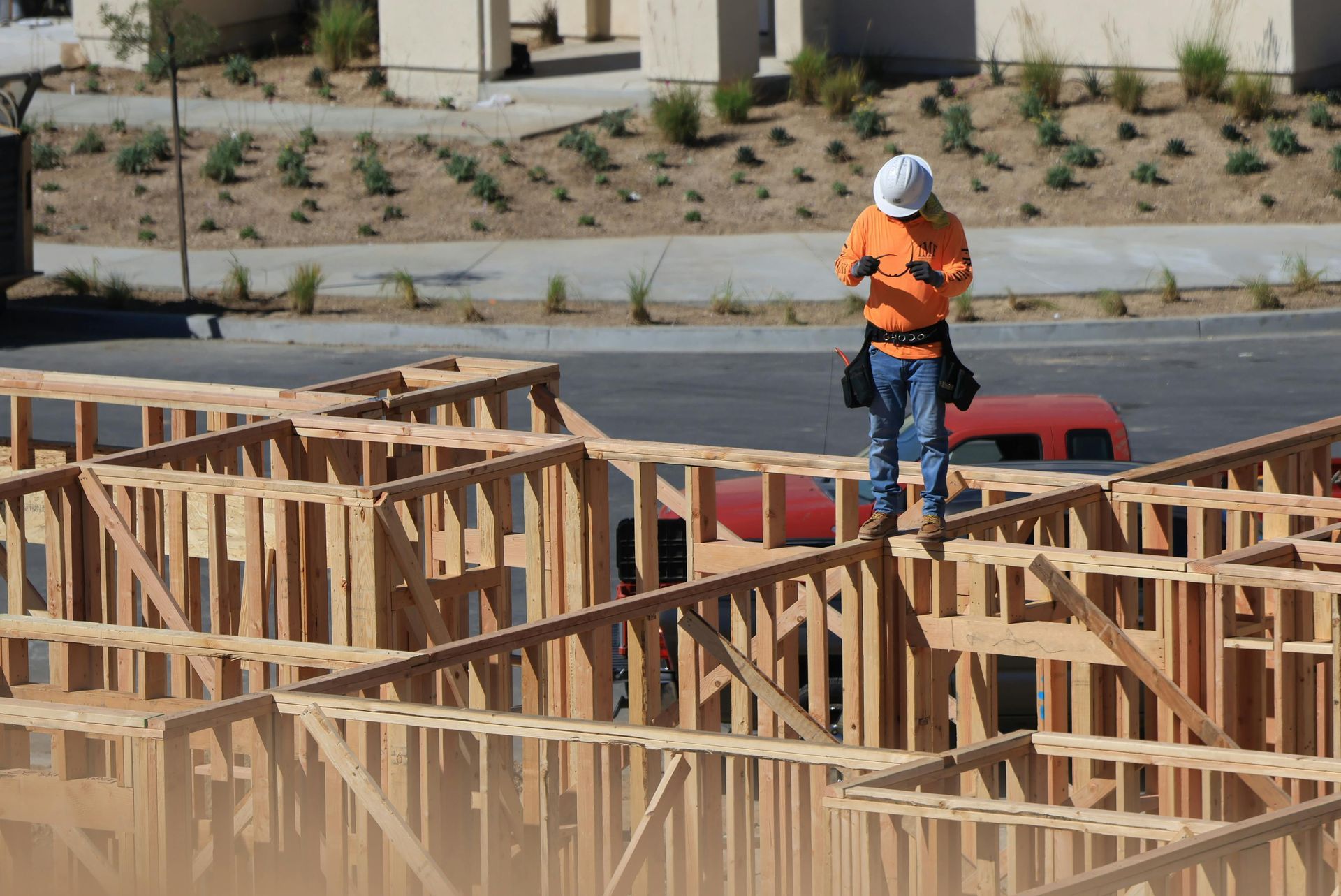Construction worker in orange vest and hard hat standing on wooden framing at a building site