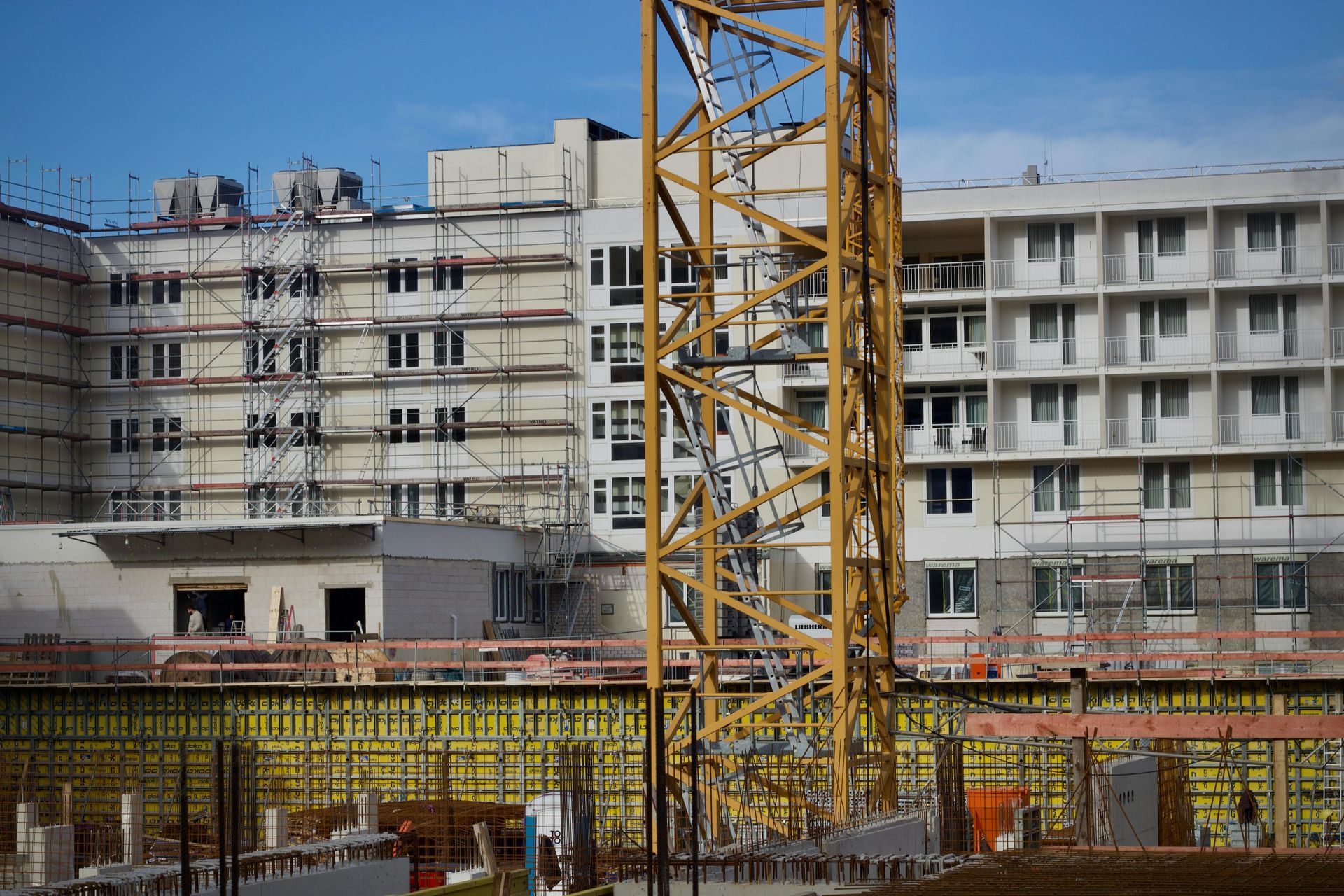 Construction site with yellow crane and partially built white apartment buildings under a clear blue sky