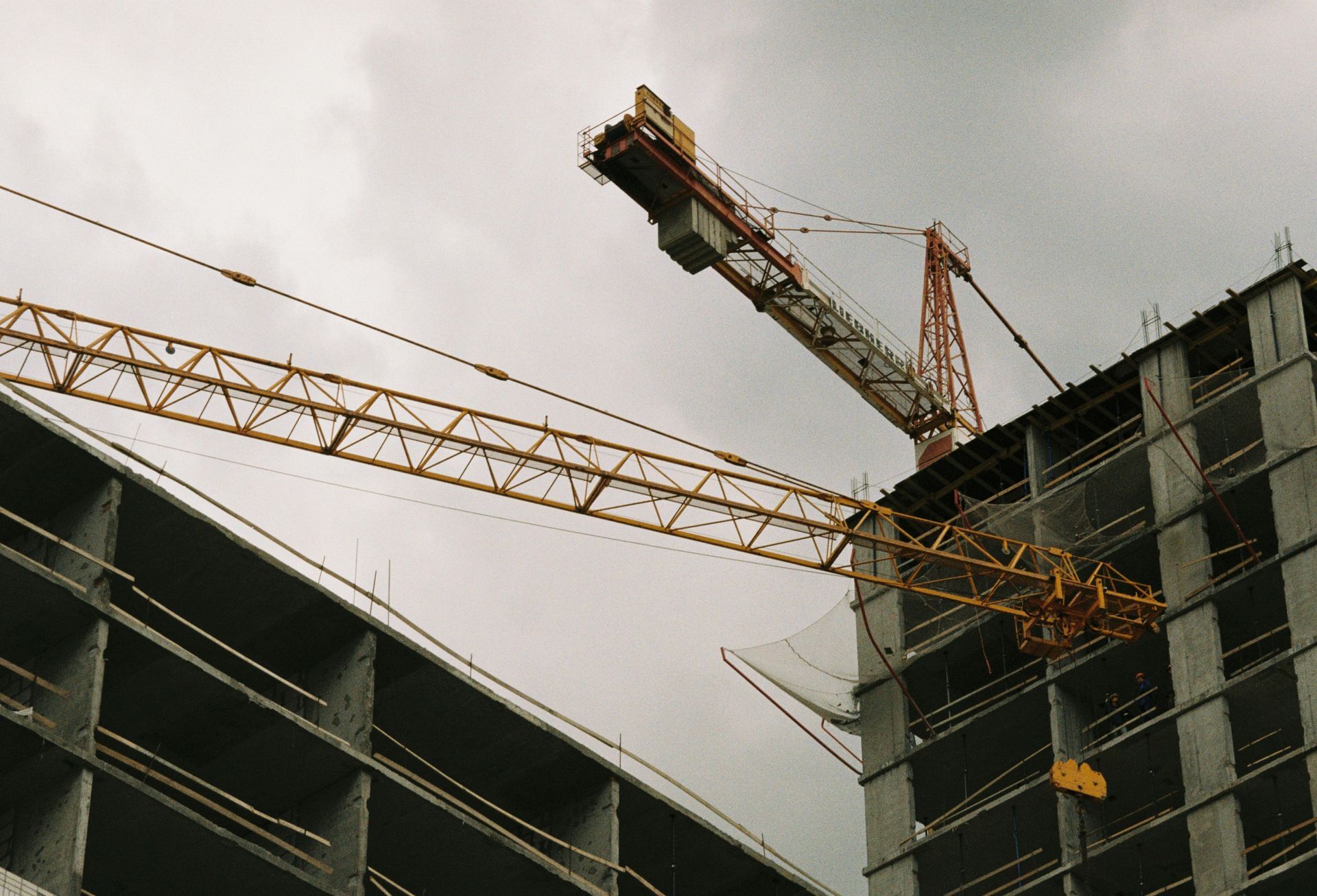 Construction cranes over unfinished high-rise buildings against a gray sky