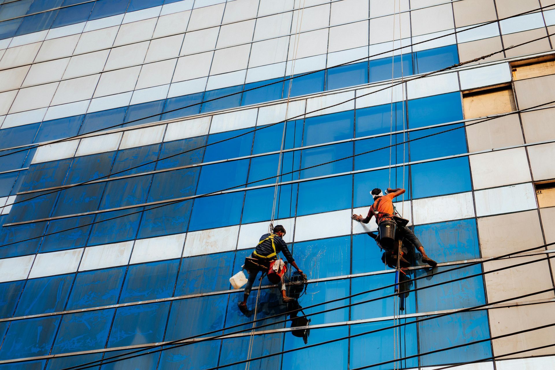 Two window cleaners on ropes cleaning a blue glass office building facade
