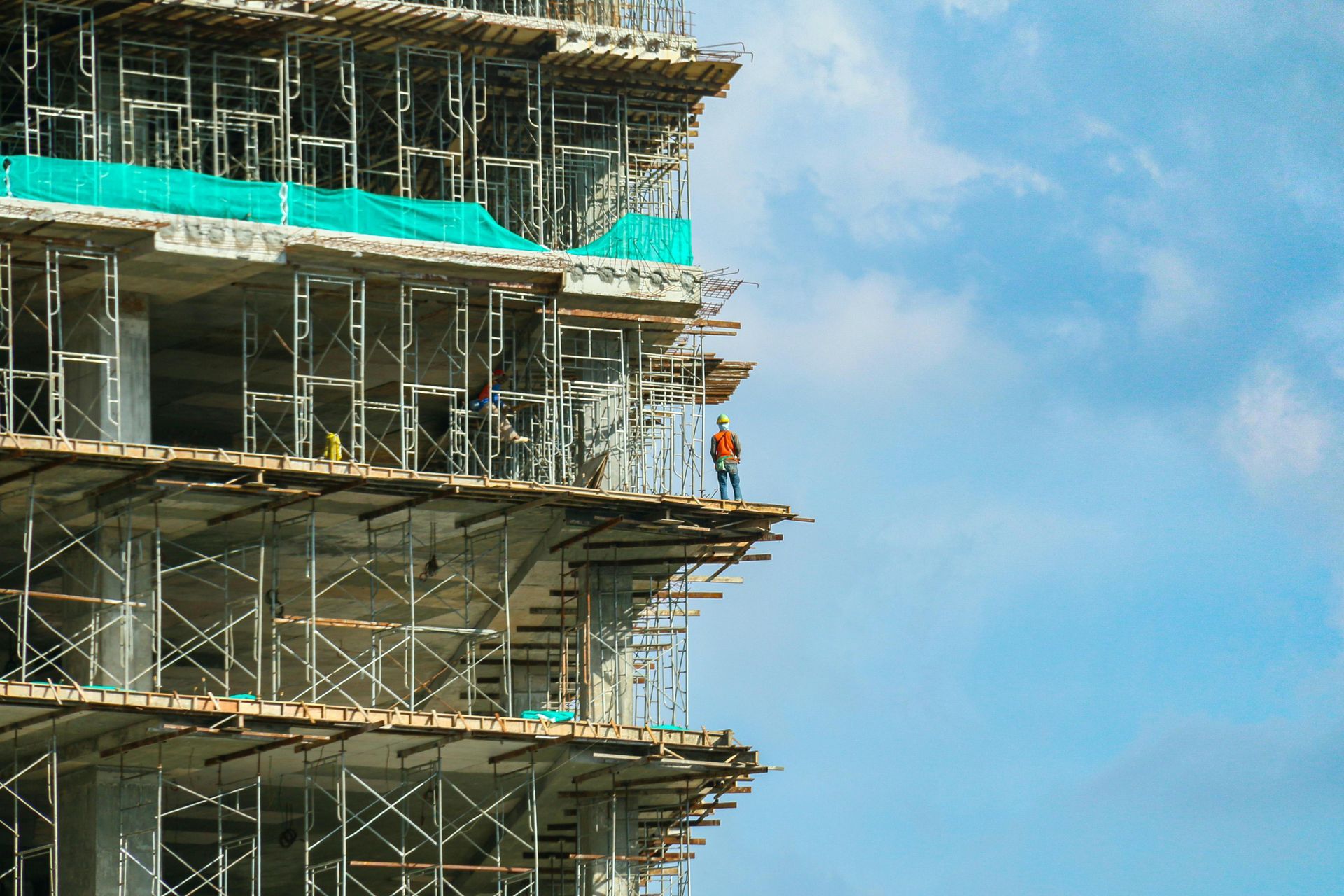 Construction site with workers on scaffolding beside a partially built high-rise against a blue sky