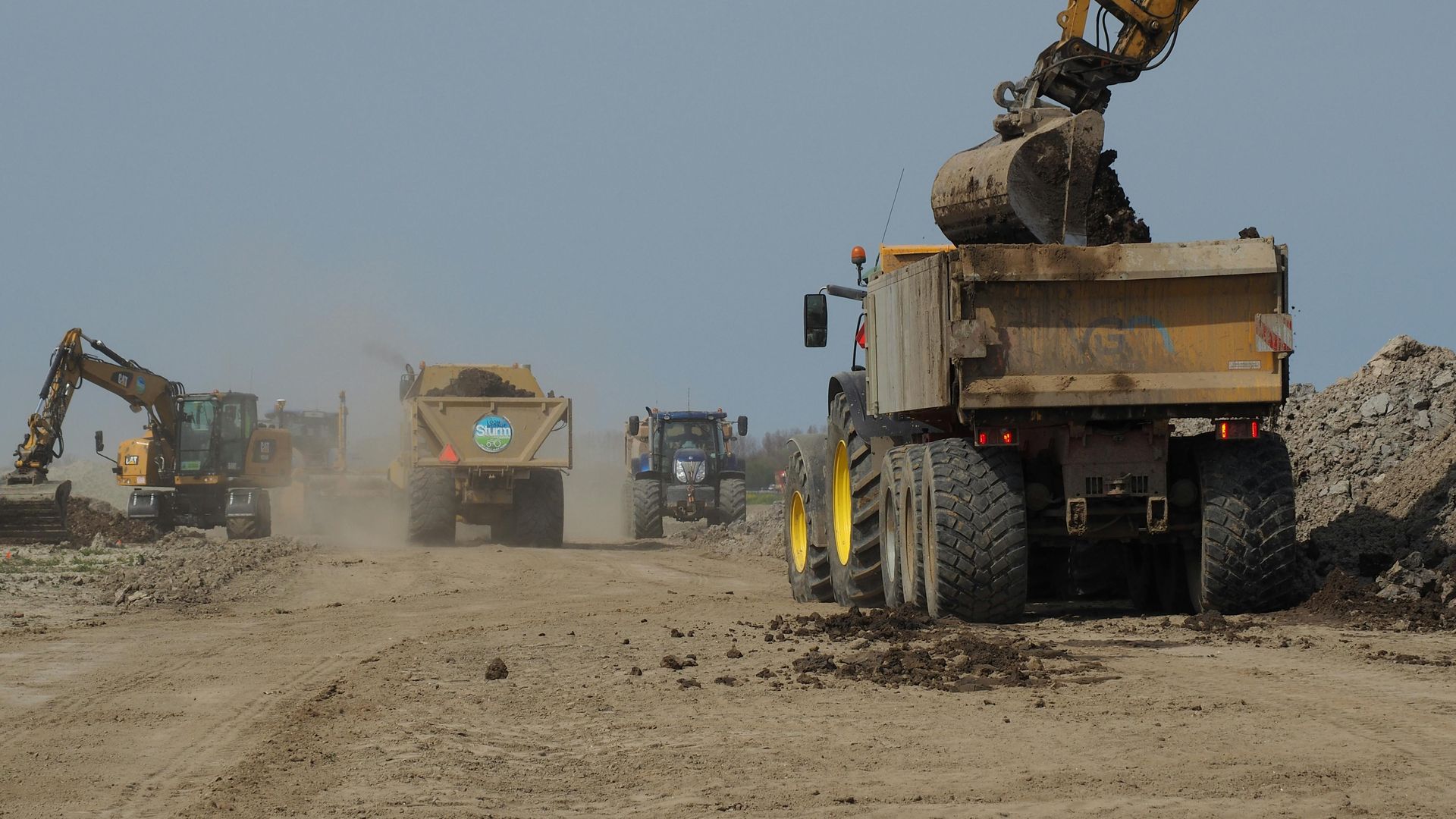 Heavy construction trucks and excavators moving dirt on a dusty site
