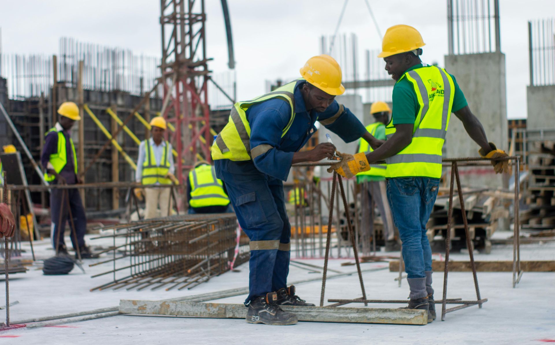 Construction workers in hard hats and safety vests bending rebar at an active building site