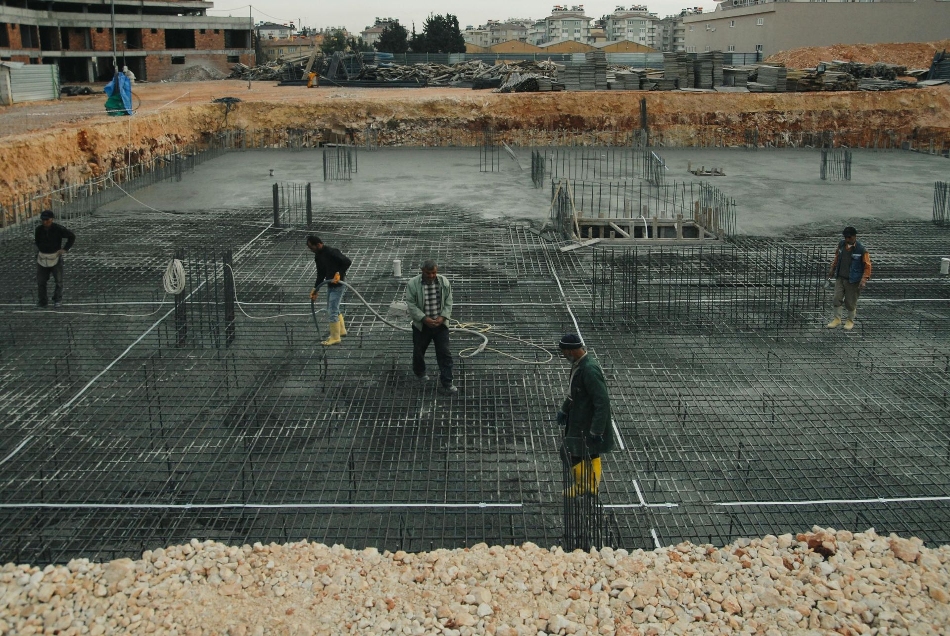 Workers installing rebar in a large concrete foundation pit at a construction site
