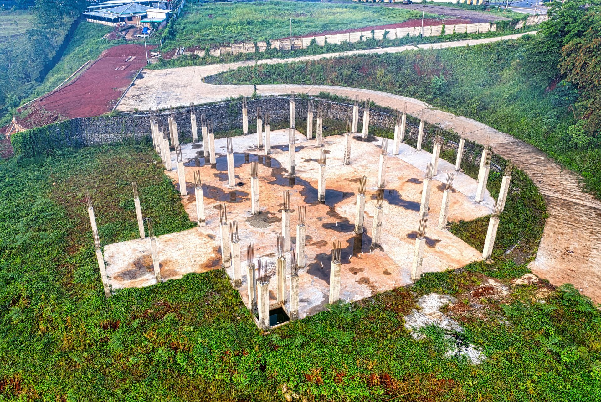 Circular concrete foundation with many columns in a grassy rural construction site, viewed from above