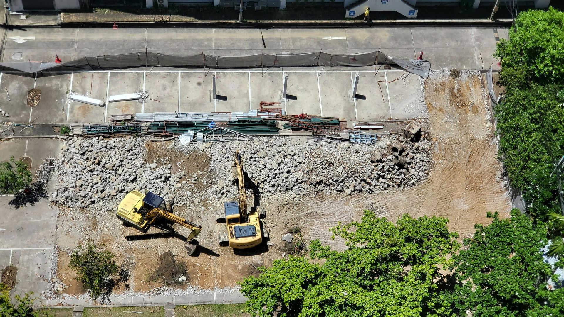 Aerial view of a demolition site with two yellow excavators clearing rubble beside a concrete slab.
