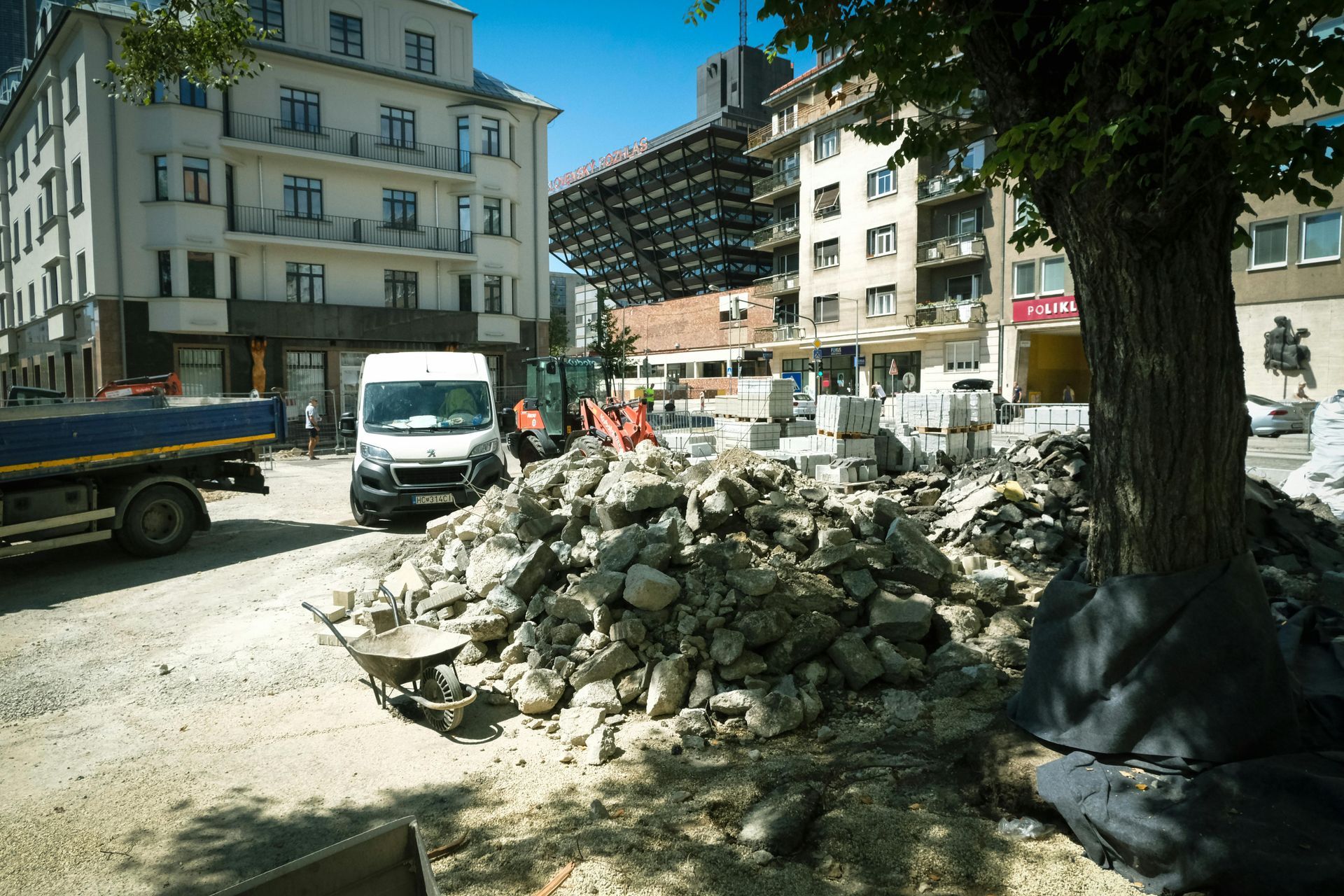 Pile of rubble on a city street beside parked vans and apartment buildings under a blue sky
