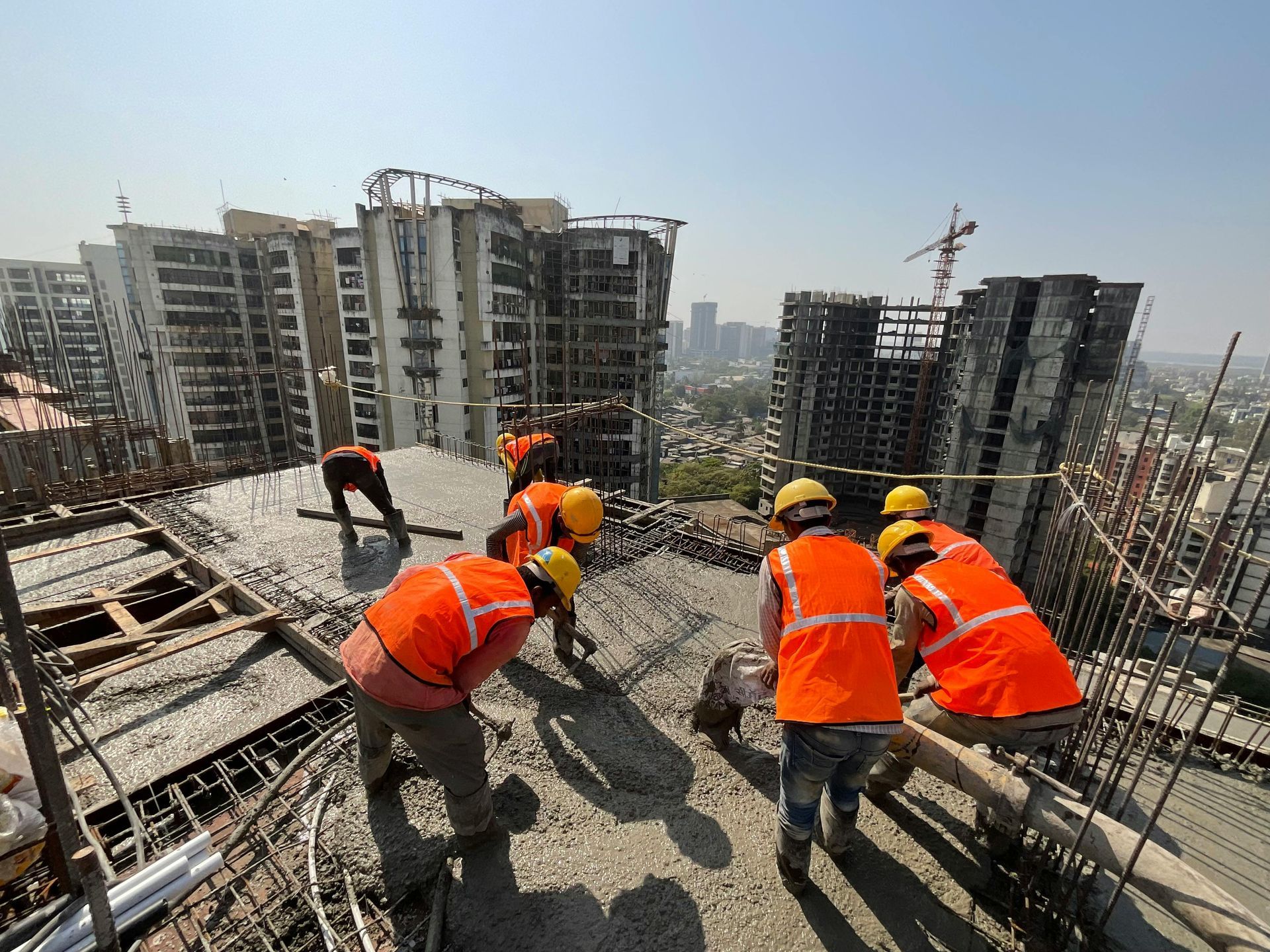 Road construction site with stacked concrete blocks, workers, and trees along a street