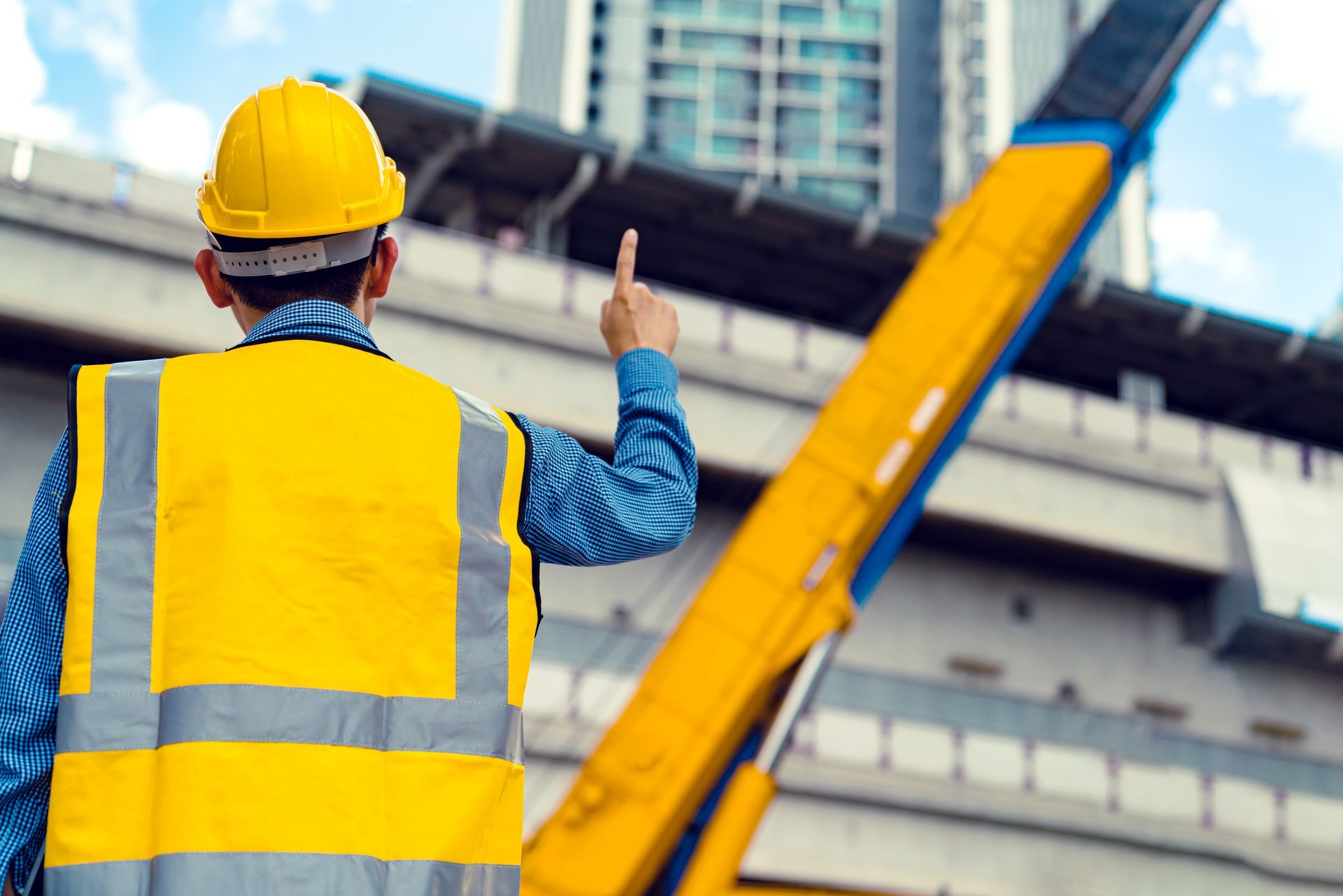 Construction worker in yellow vest and hard hat directing work at a bridge site