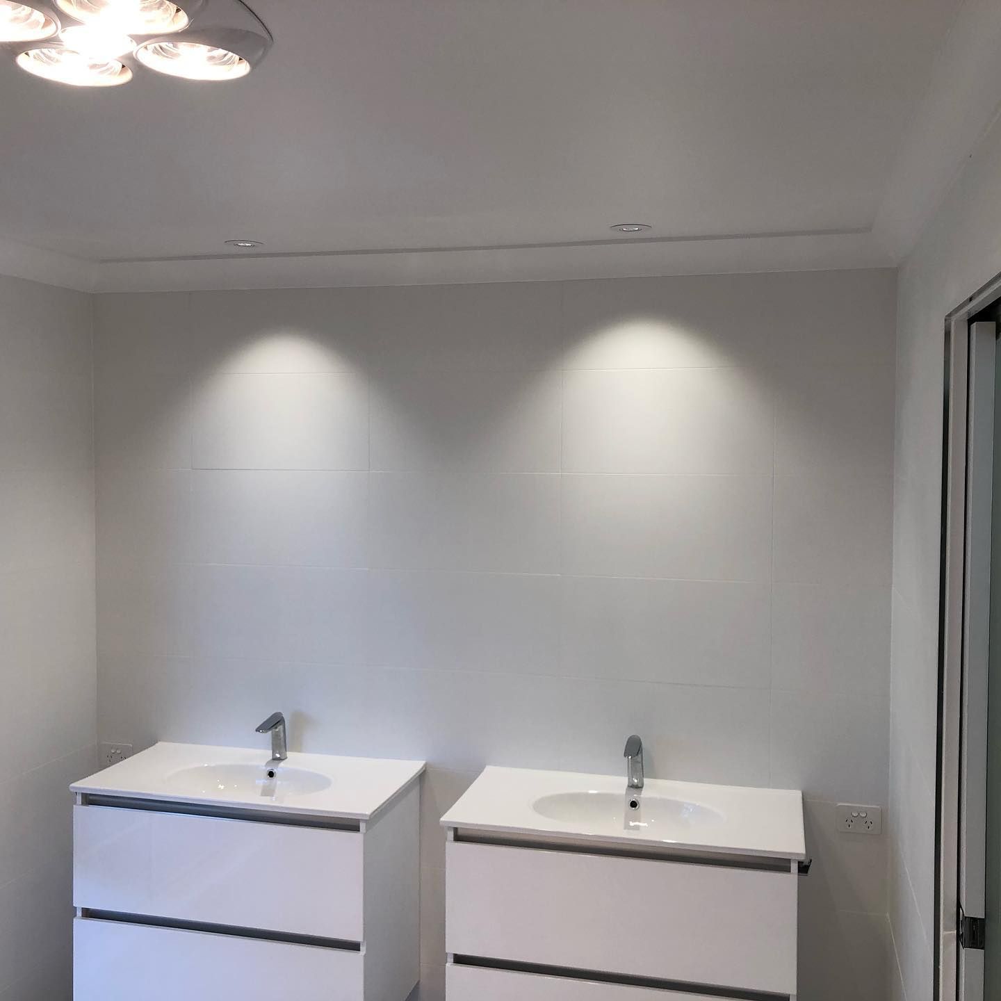 Two white bathroom vanities with sinks, under spotlight.