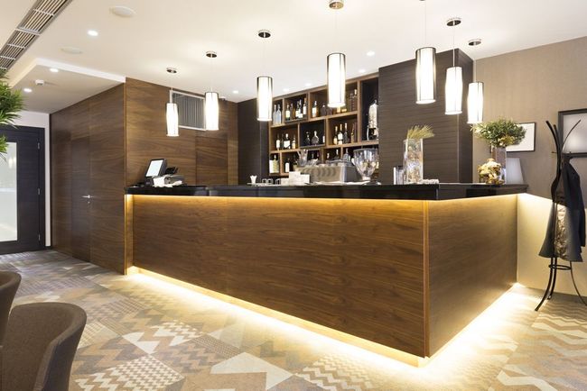 Bar with wood paneling, lit from below, with overhead pendant lights and bottles on shelves.