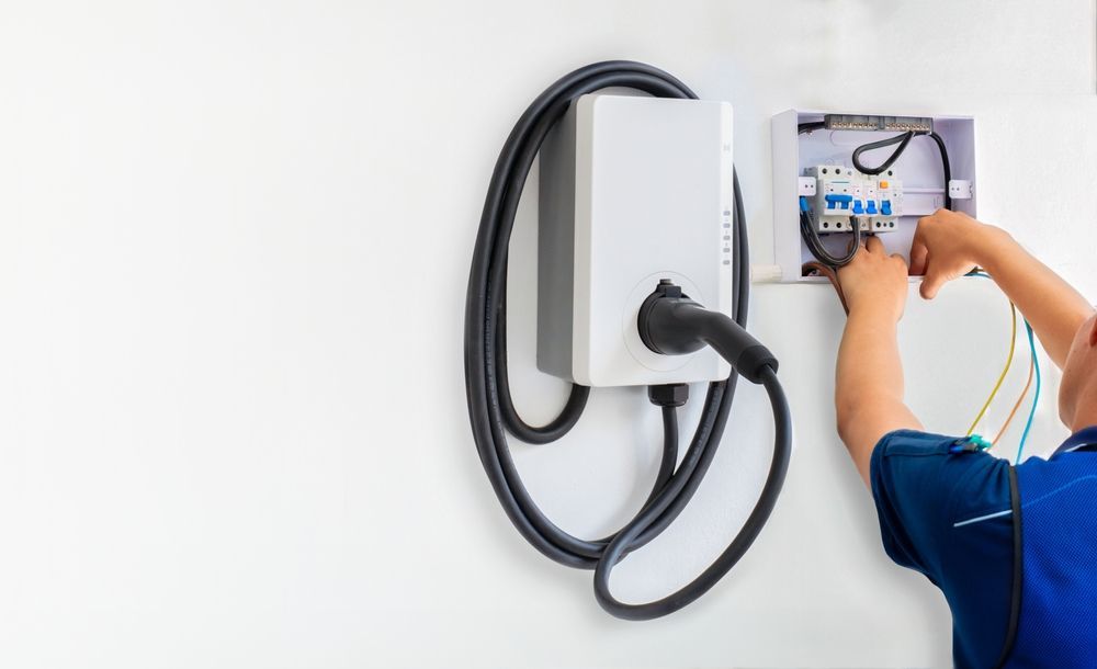 Electrician installing wiring for an EV charger on a white wall.