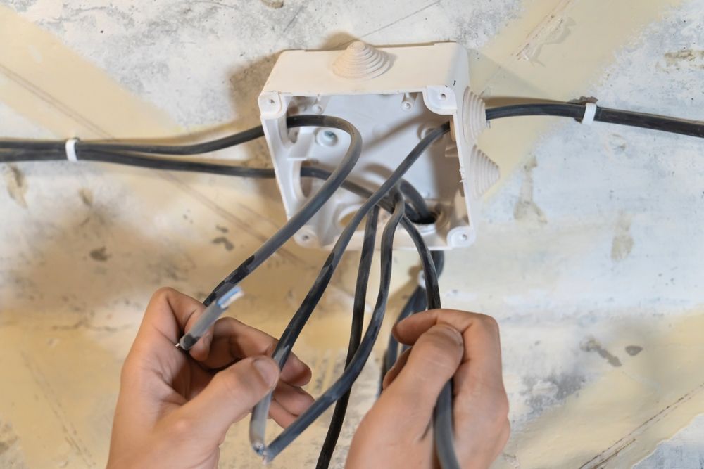 Man on ladder holding a coil of black cable, smiling in a room.