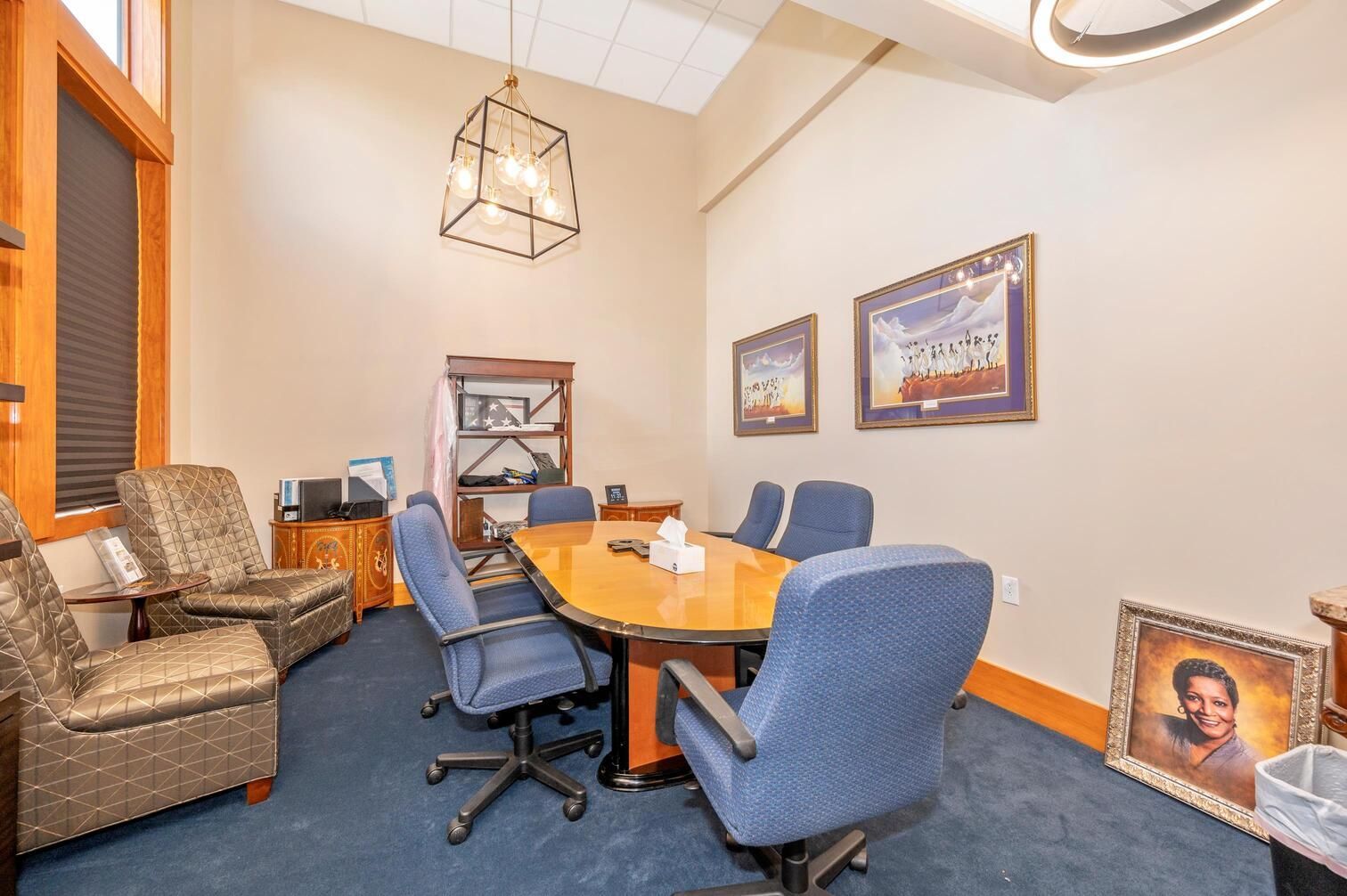 Conference room with blue chairs, wooden table, beige walls, and framed artwork.