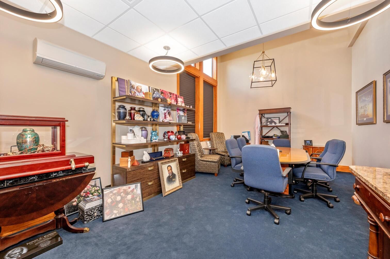 A cozy office with blue chairs, wooden table, shelves, and red pool table cover under circular ceiling lights.