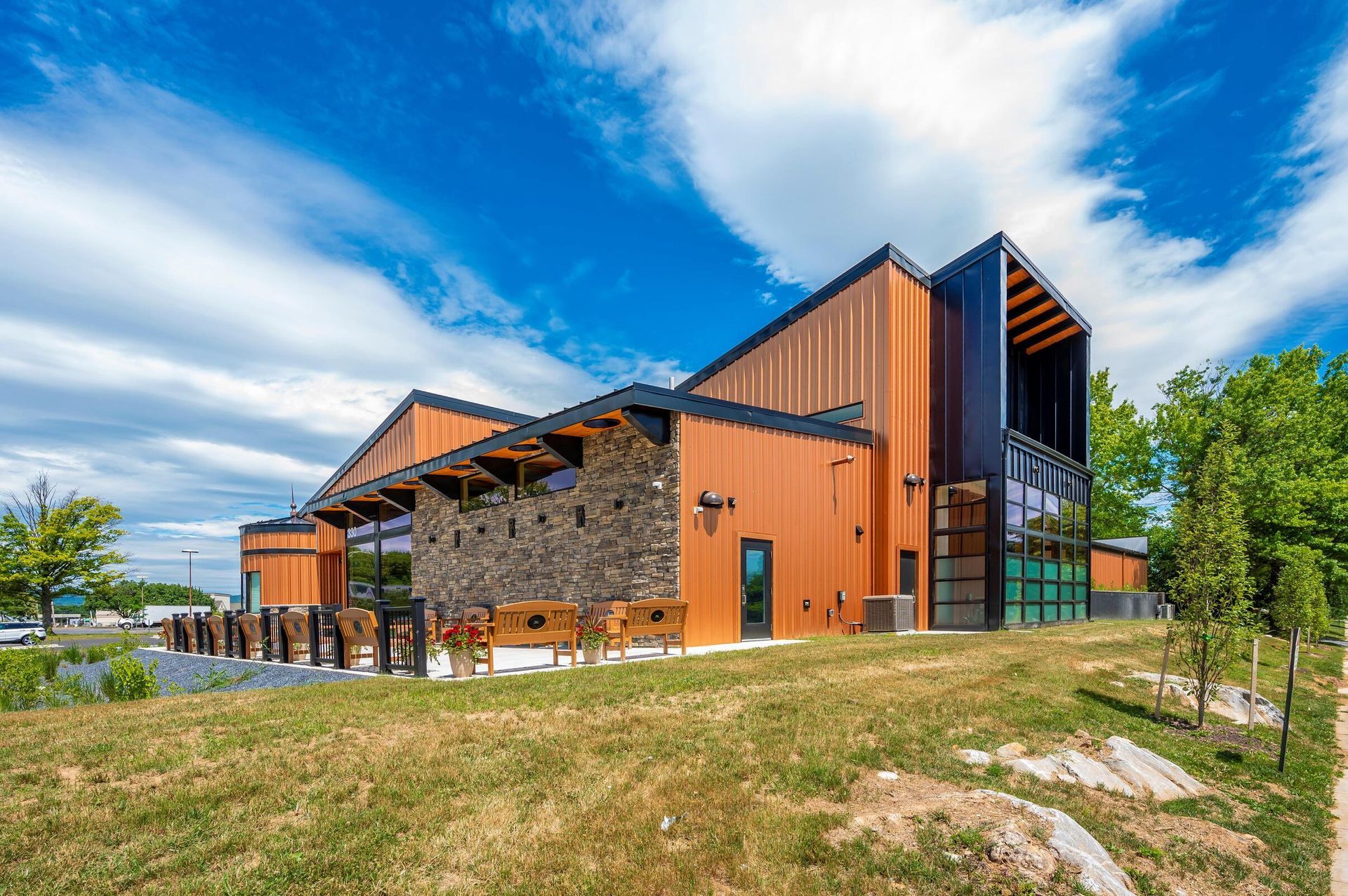 Modern building with orange and stone facades under a bright blue sky, set in a grassy landscape