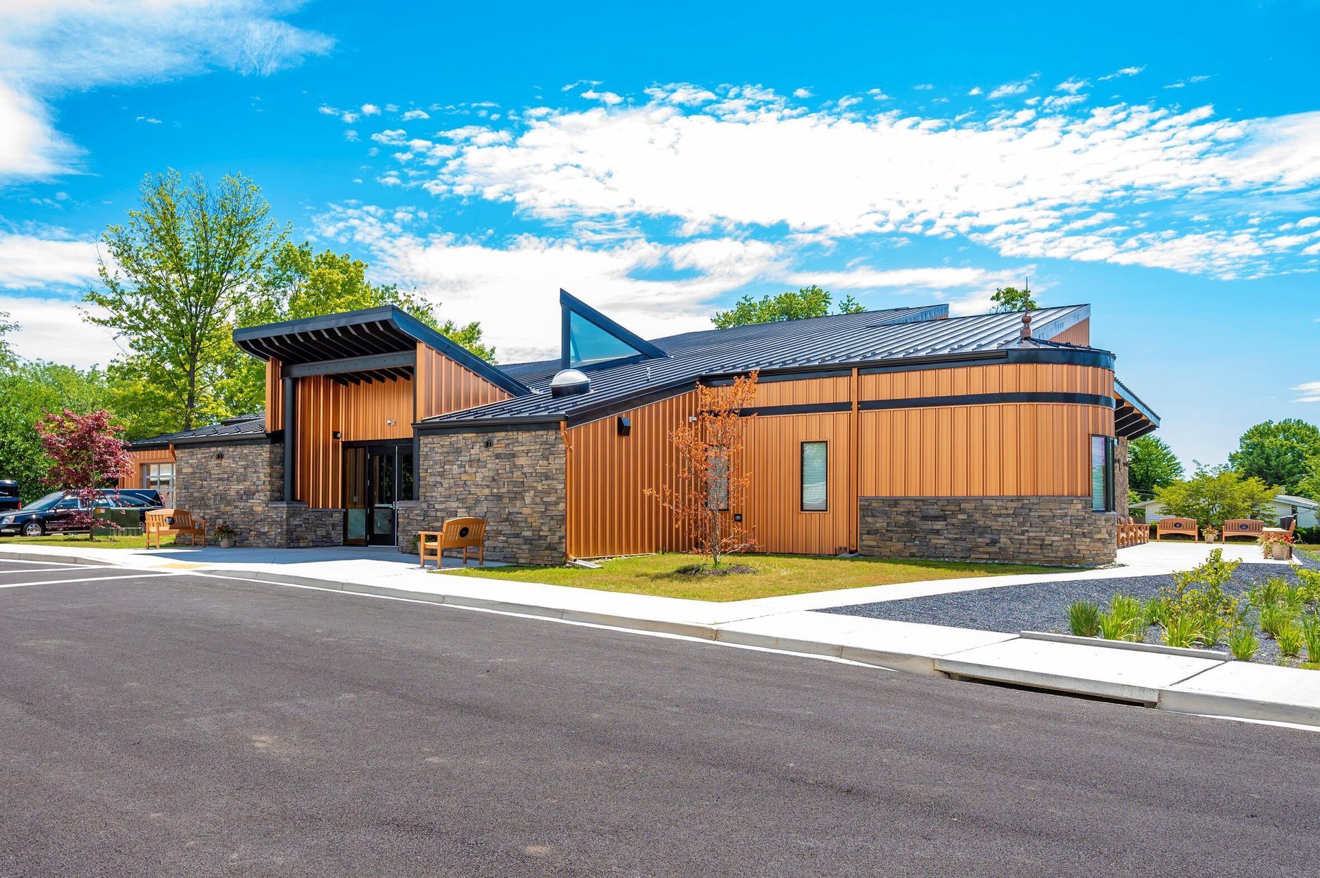 Modern building with wood and stone exterior beside a paved road under a bright blue sky