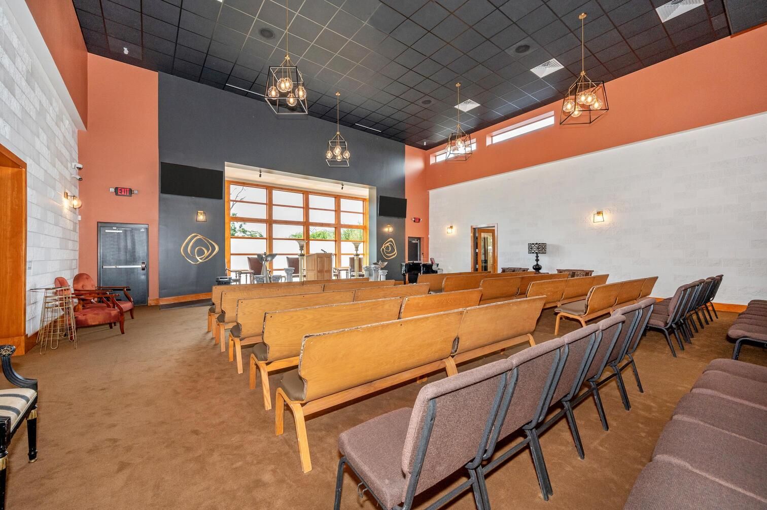 Empty church sanctuary with rows of wooden pews, orange walls, and a high black ceiling