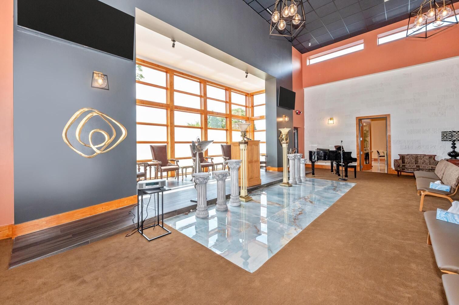Modern lobby with glass doors, high ceilings, blue accent wall, and carpeted seating area