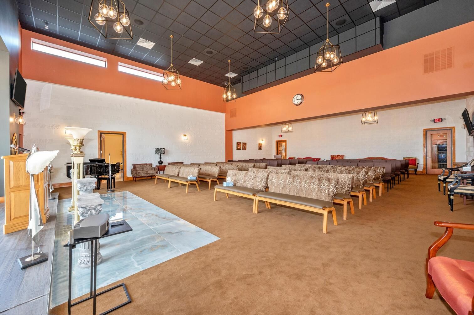Large church sanctuary with rows of pews, orange walls, and high ceiling lights