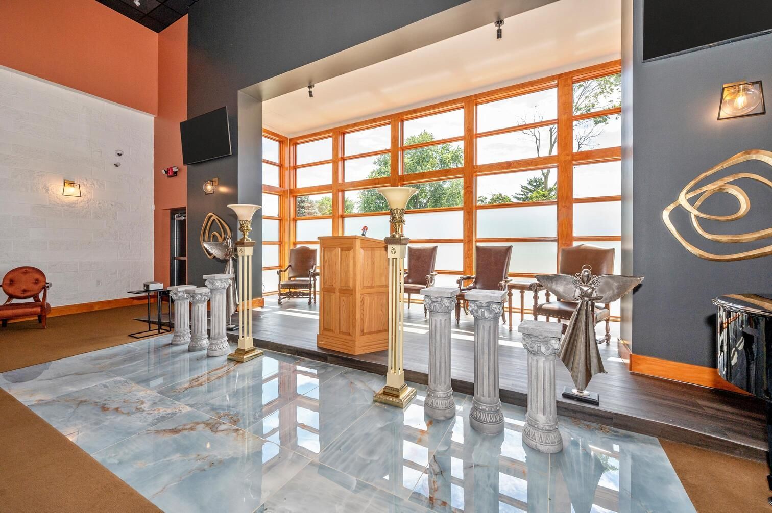 Modern lobby with glossy floor, wooden reception desk, metal chairs, and large sunlit windows