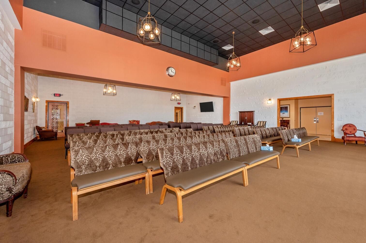 Empty church sanctuary with rows of patterned benches, tan carpet, white walls, and wooden doors