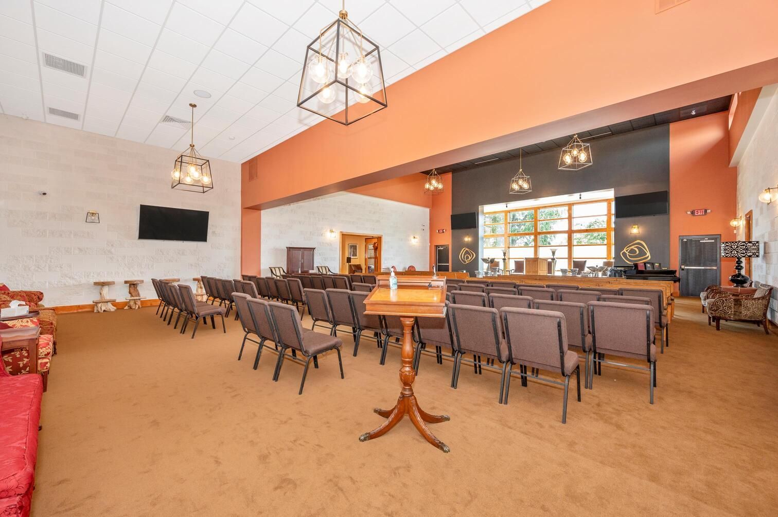 Spacious banquet hall with rows of chairs, wooden tables, and orange-accented walls under hanging lights