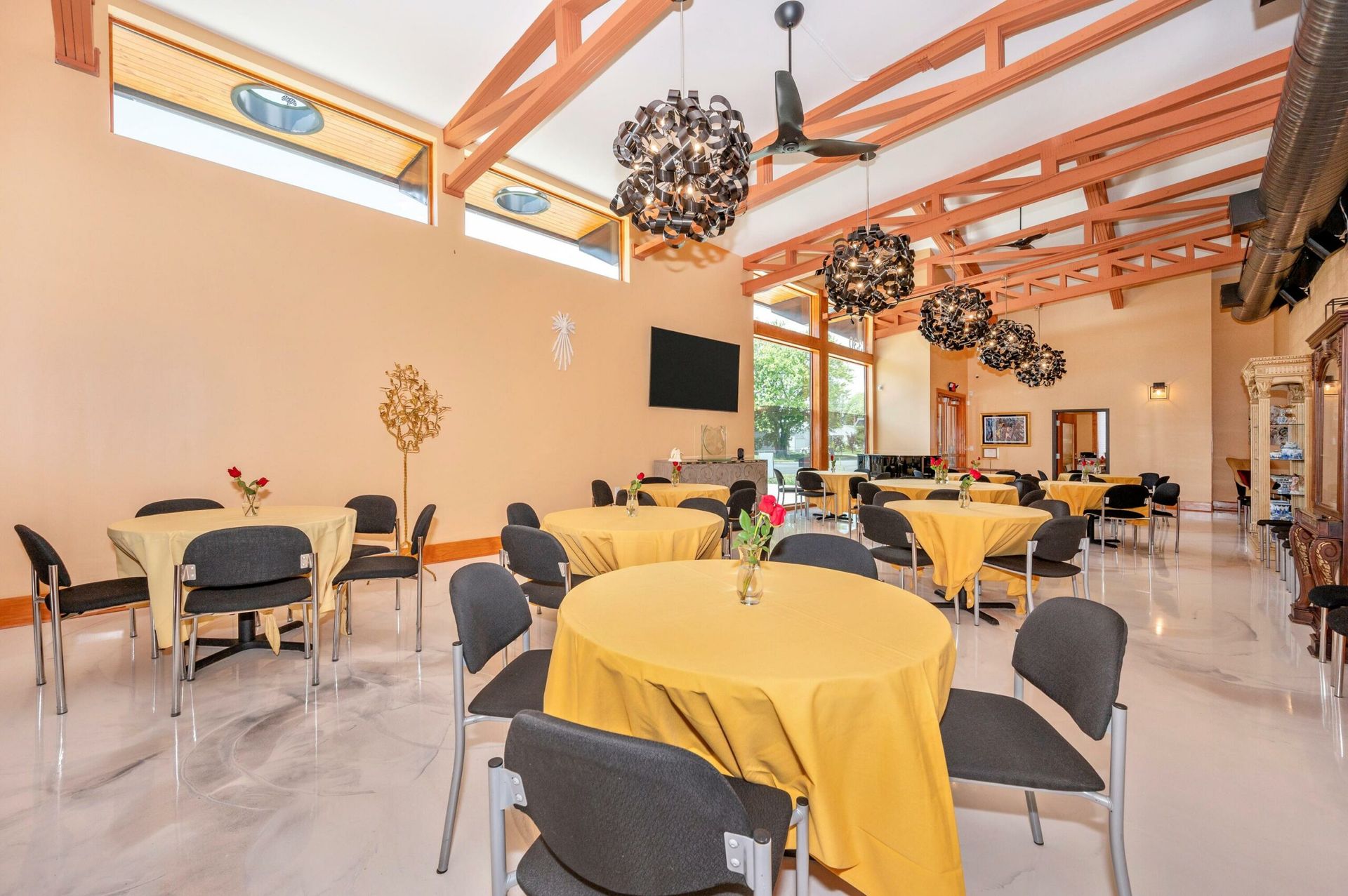 Bright café dining room with yellow tablecloths, black chairs, and wooden ceiling beams