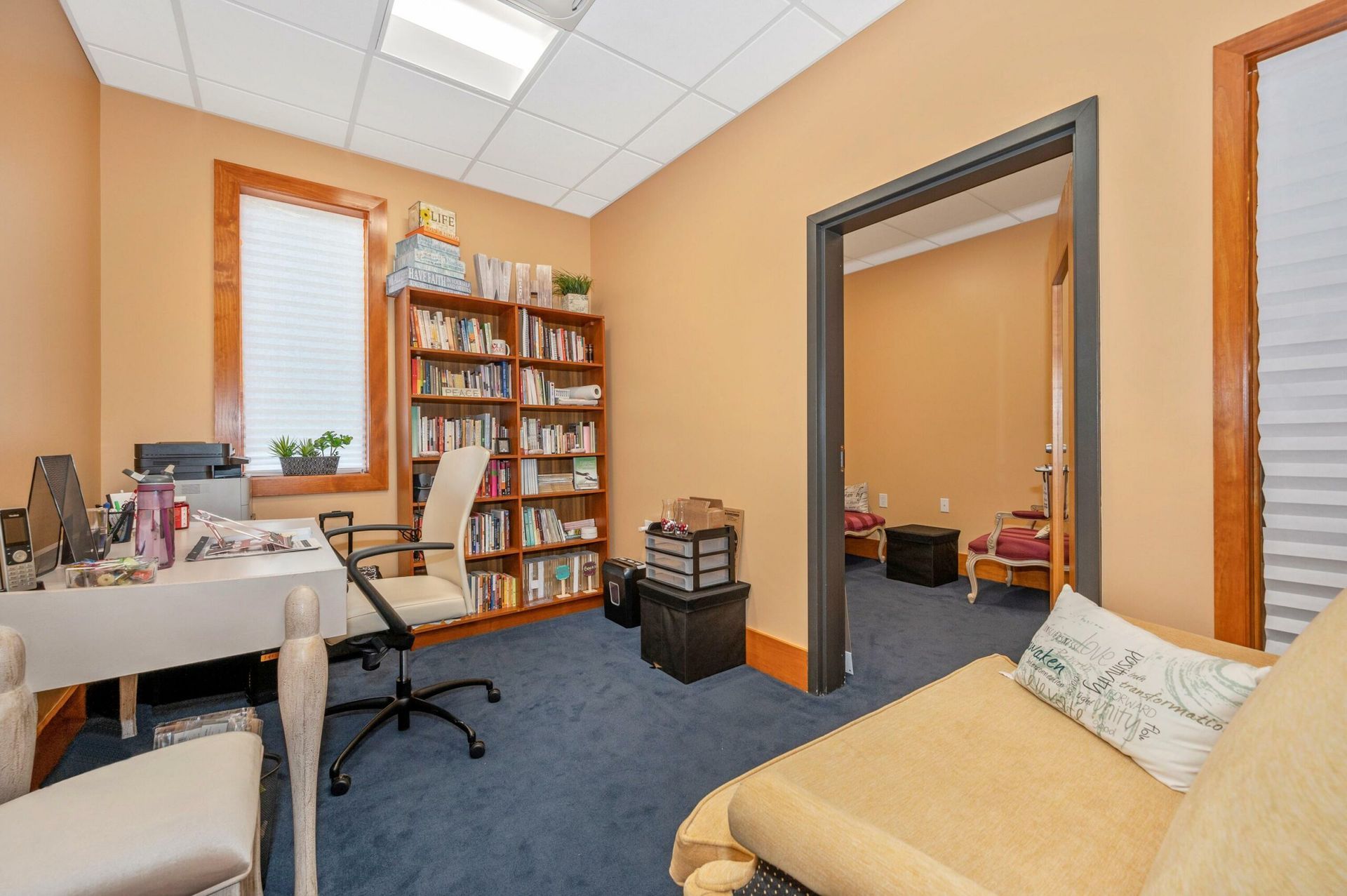 Office with desk, bookshelves, beige couch, blue carpet, and open doorway on orange walls