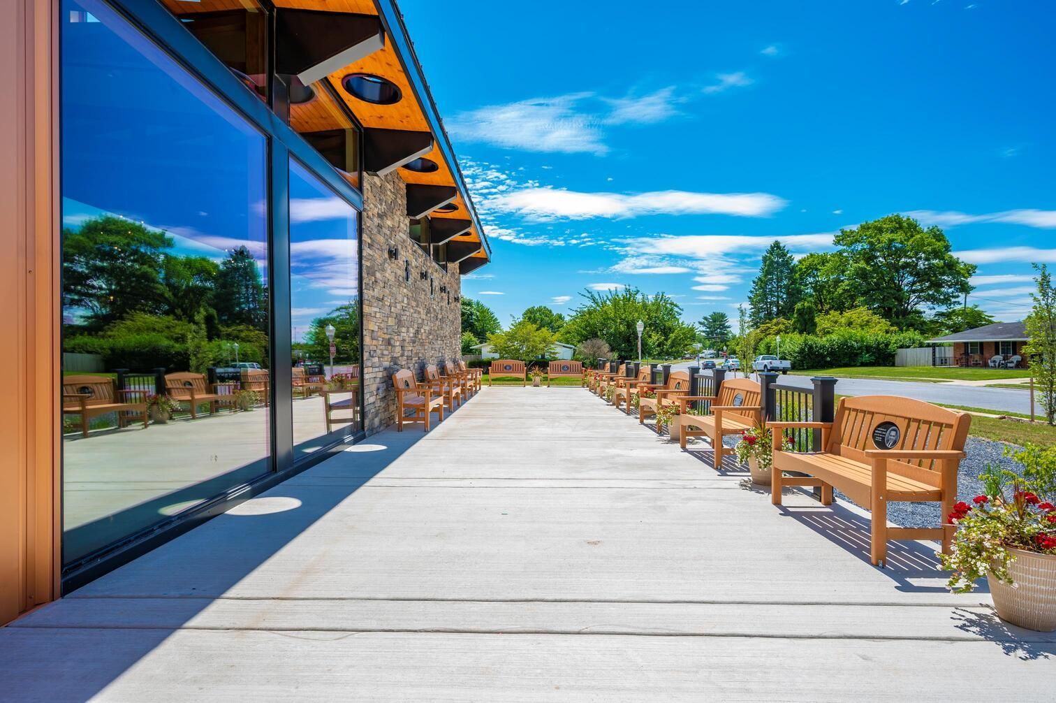 Sunny outdoor patio with wooden chairs along a stone building and a long concrete walkway