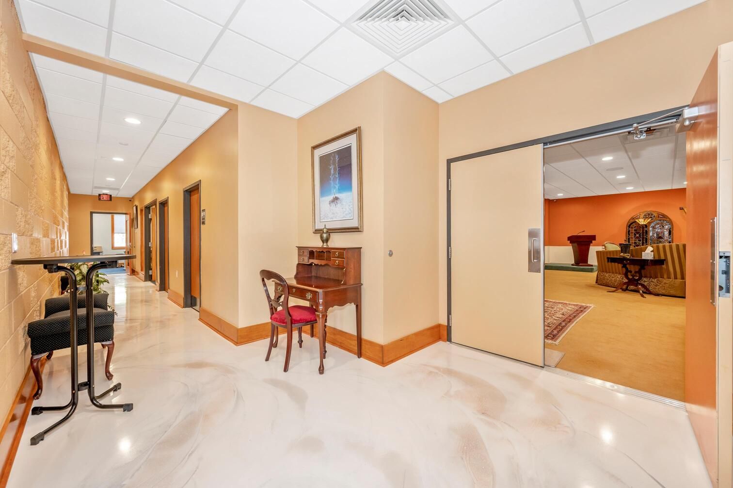 Bright office hallway with cream walls, marble floor, and an open doorway to a warm-toned conference room.