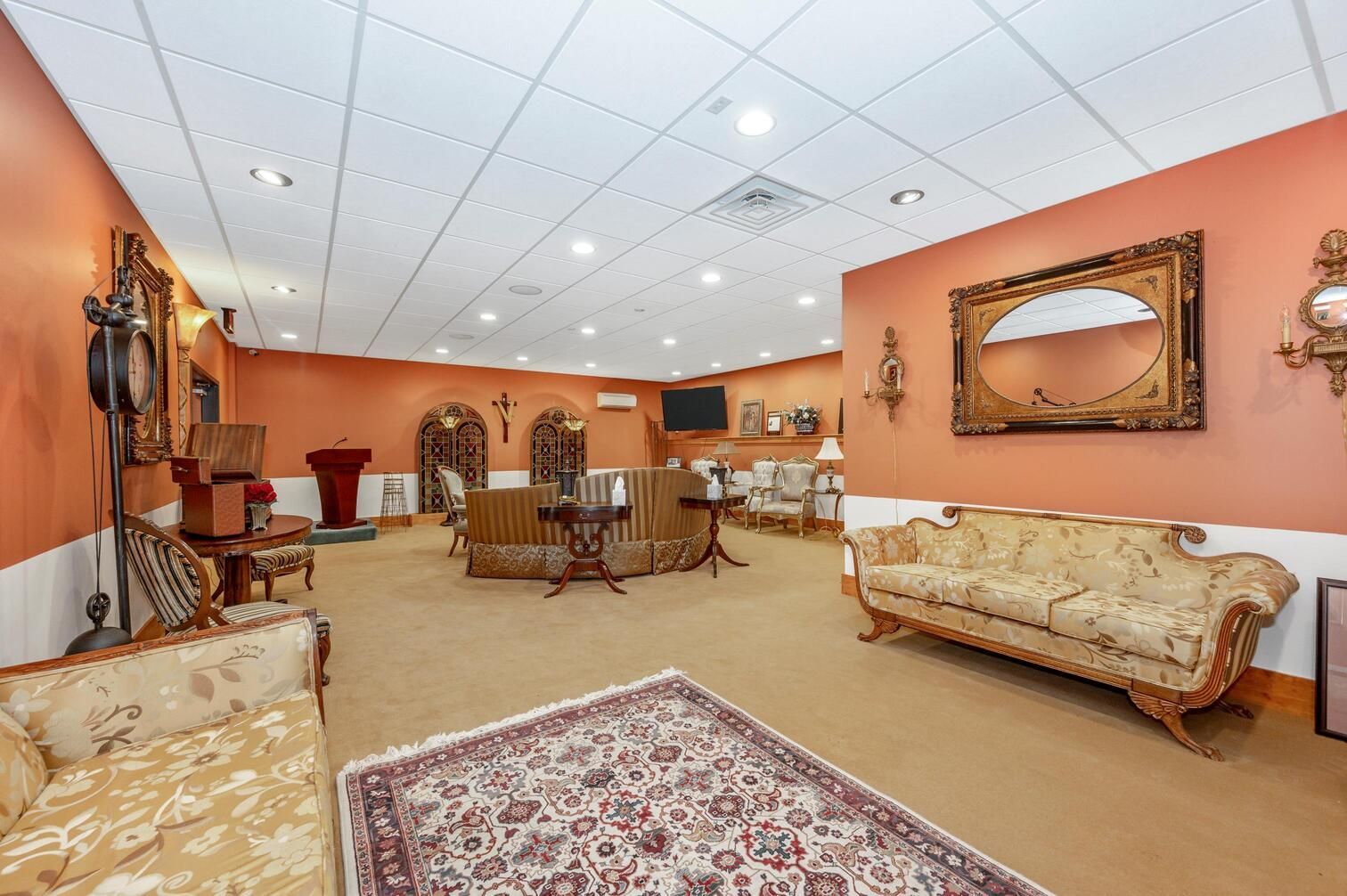 Elegant living room with orange walls, beige sofas, patterned rug, and chandelier ceiling lights.