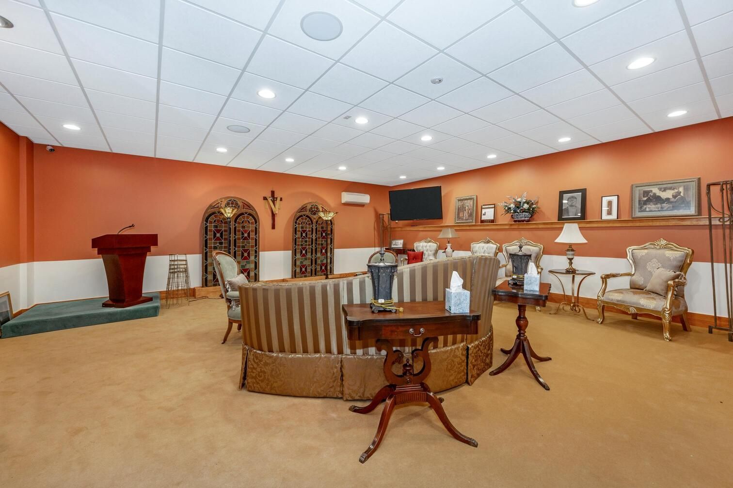 Elegant waiting room with beige carpet, orange walls, white chairs, a sofa, and framed art