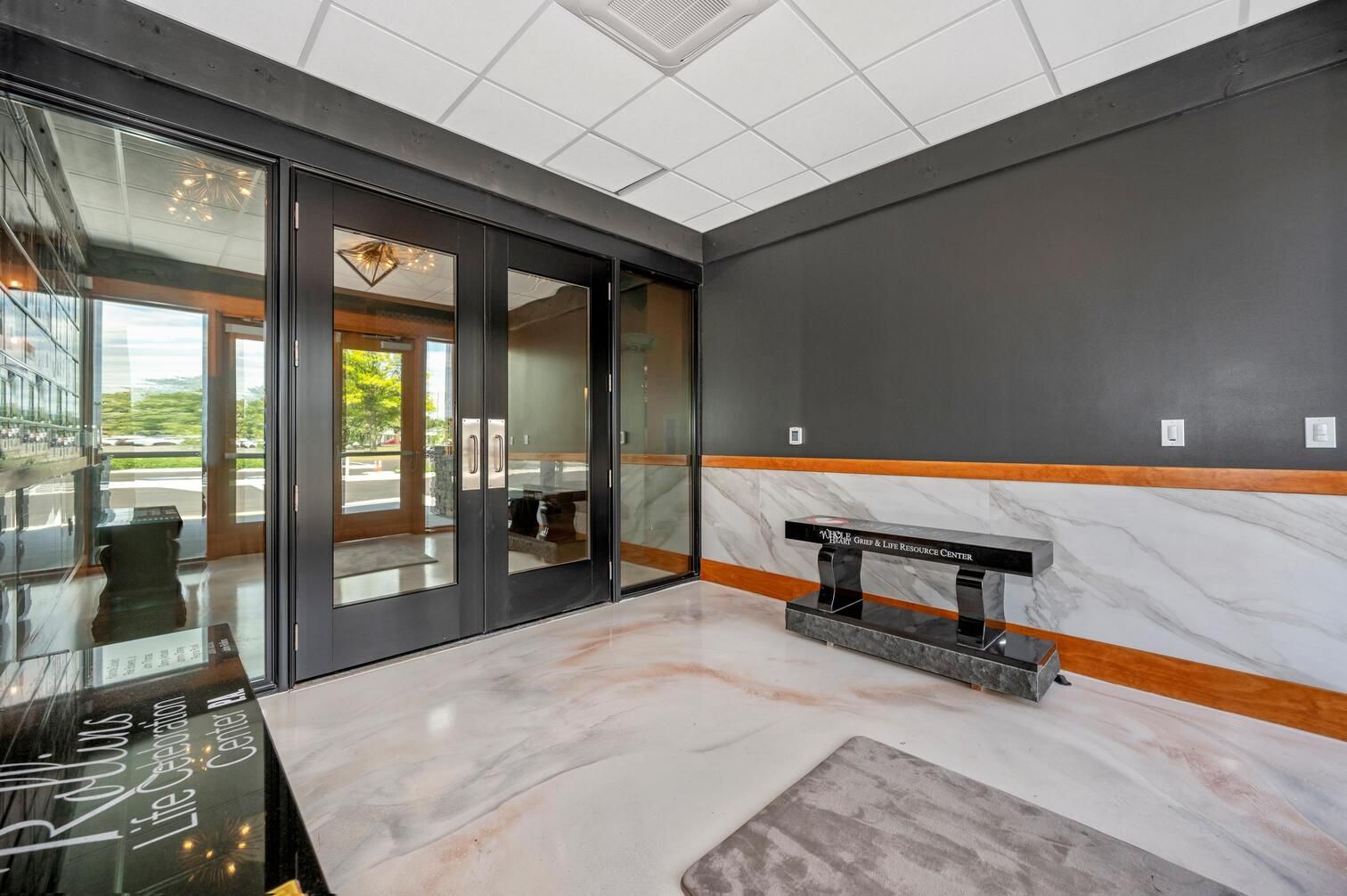 Modern lobby with glass doors, gray walls, marble floor, and a bench near the entrance