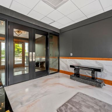 Modern lobby entry with glass doors, dark walls, marble floor, and a stone bench