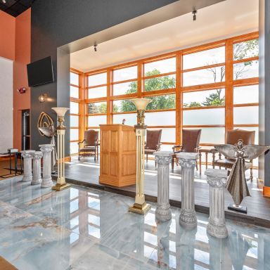 Modern church interior with wooden altar, silver railings, and large orange-framed windows