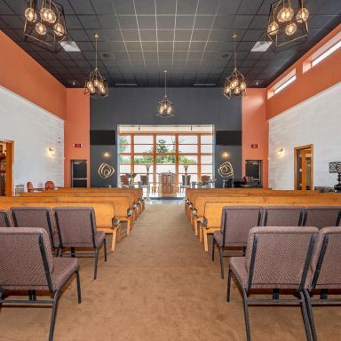 Modern church sanctuary with wooden pews, black ceiling, hanging lights, and a bright glass entrance at the back
