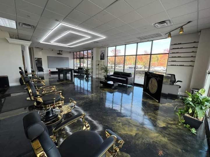 Barbershop interior with black and gold chairs, shiny black floor, large windows, and a square ceiling light.