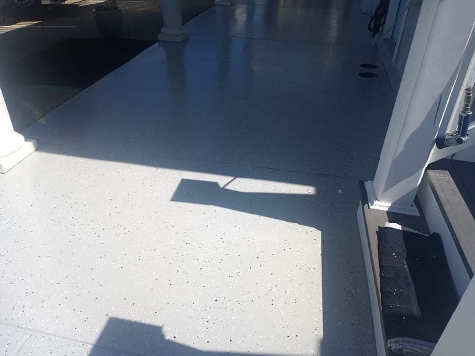 Gray speckled concrete porch floor with shadows cast by a railing.